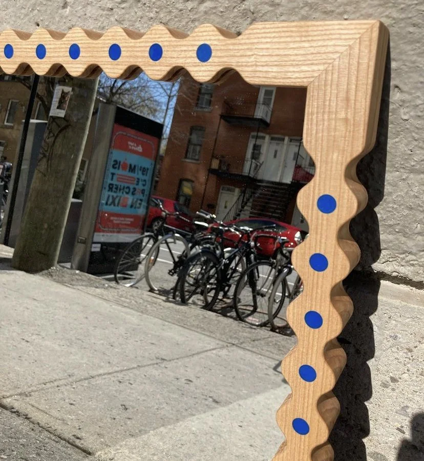 Close-up of a wooden frame with blue dots on its top edge, reflecting a street scene with bicycles, parked cars, and buildings.