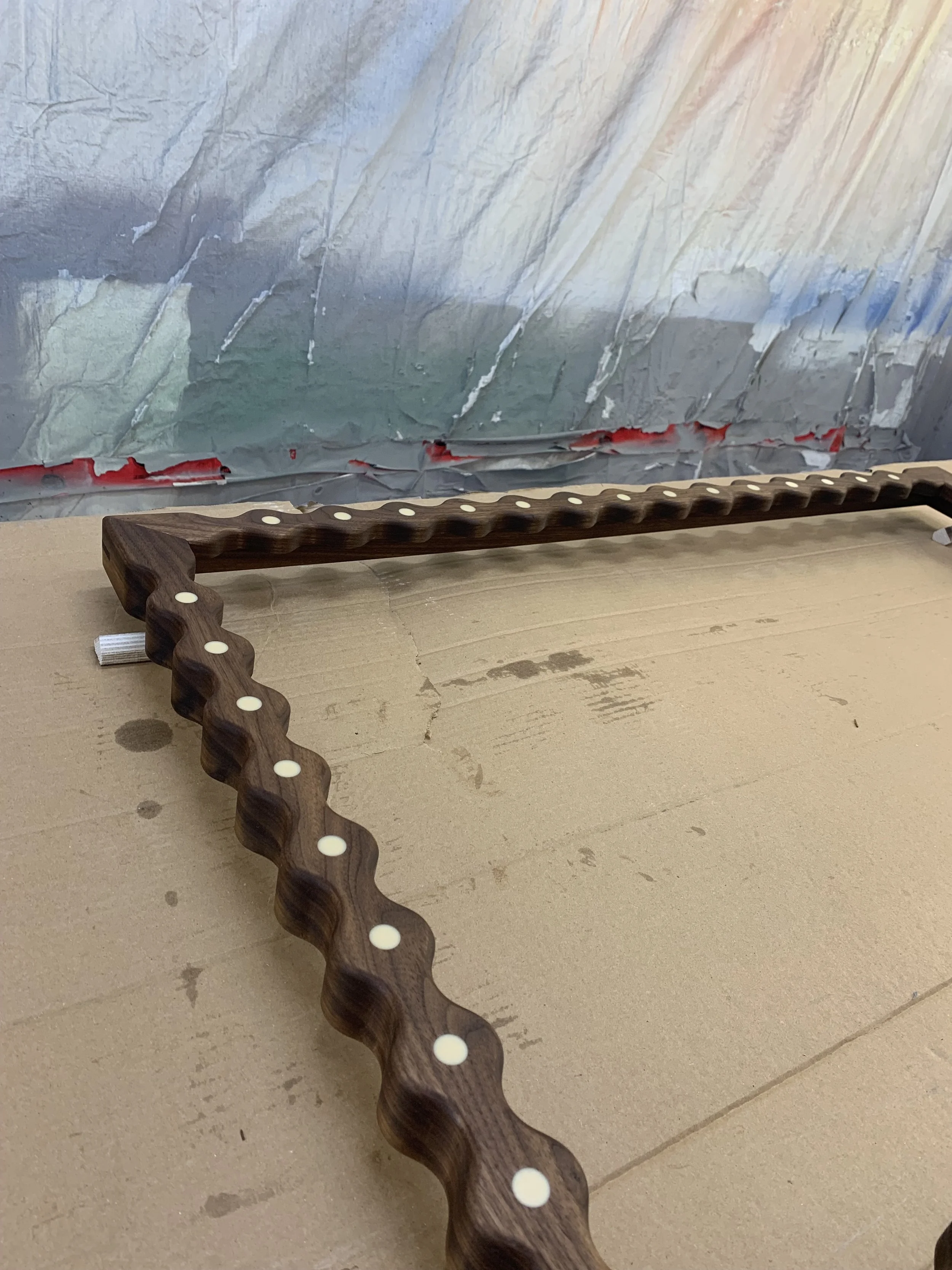 Wooden object with evenly spaced white dots lying on a beige surface in front of a metallic background.