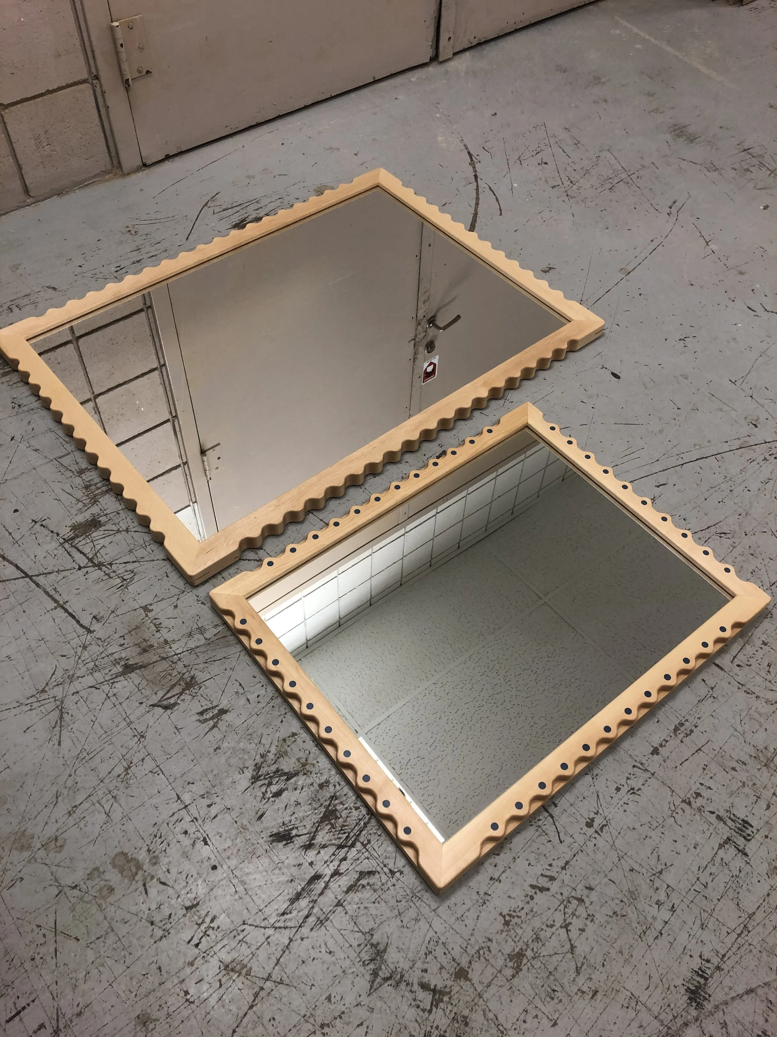 Two square mirrors with wooden frames placed on a scratched gray concrete floor, leaning against a wall.