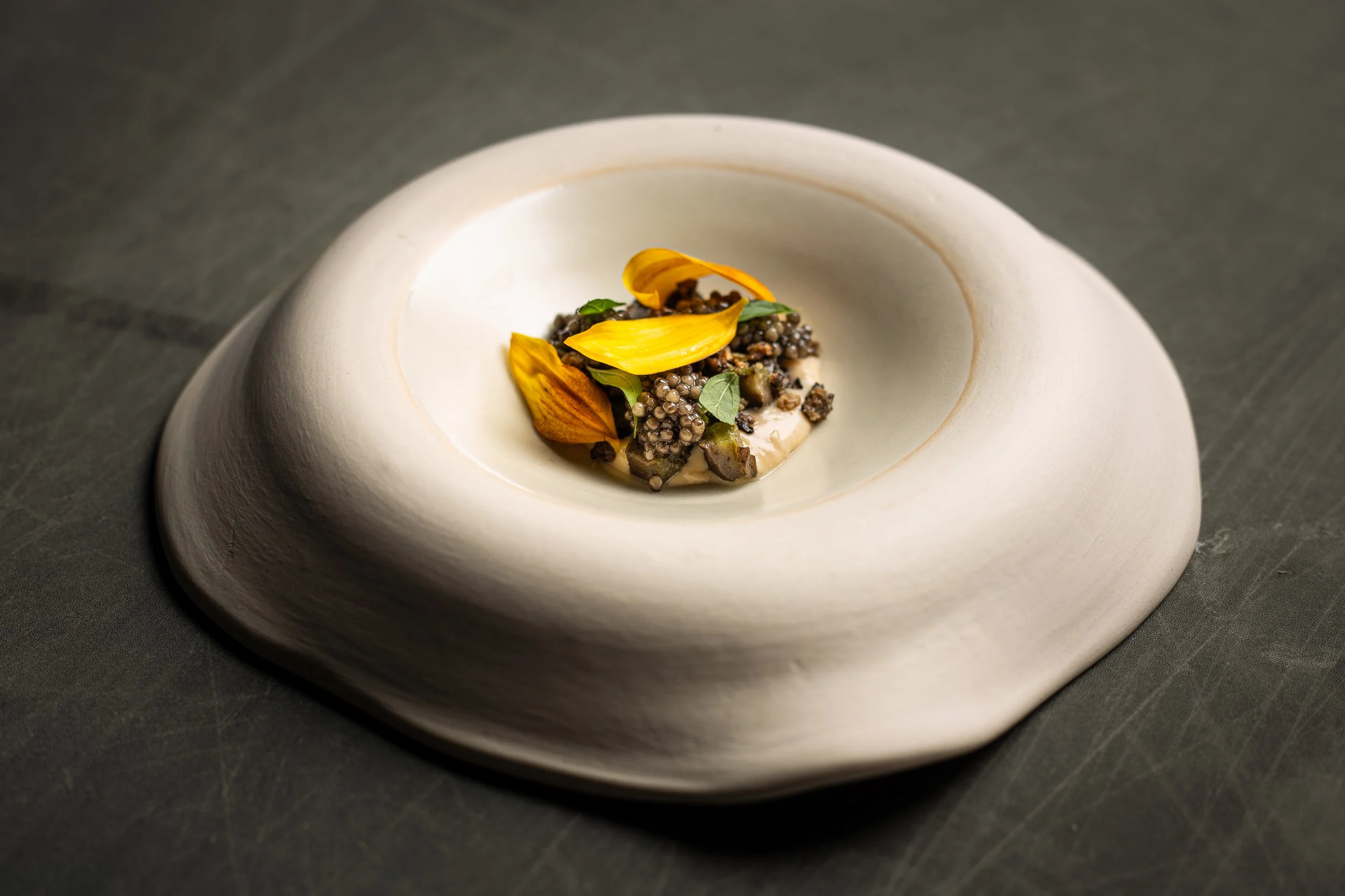 Elegant plate with a gourmet dish featuring black caviar, garnished with edible flower petals and small green herbs, served on a modern white plate.