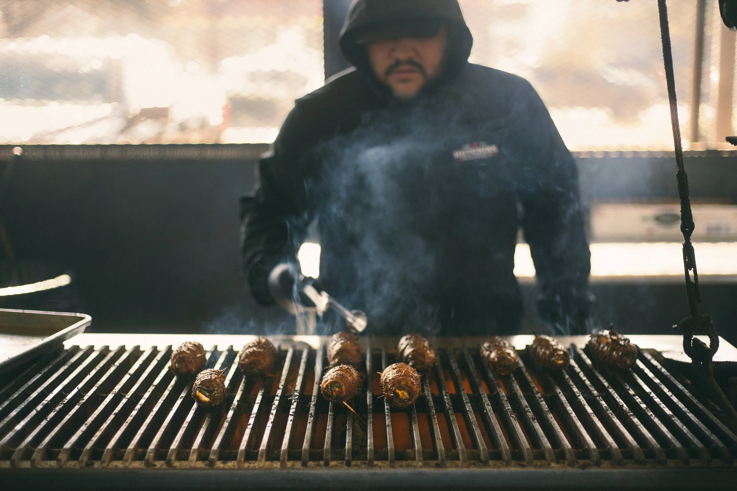 A man grilling skewered food on a barbecue grill with smoke in the background.