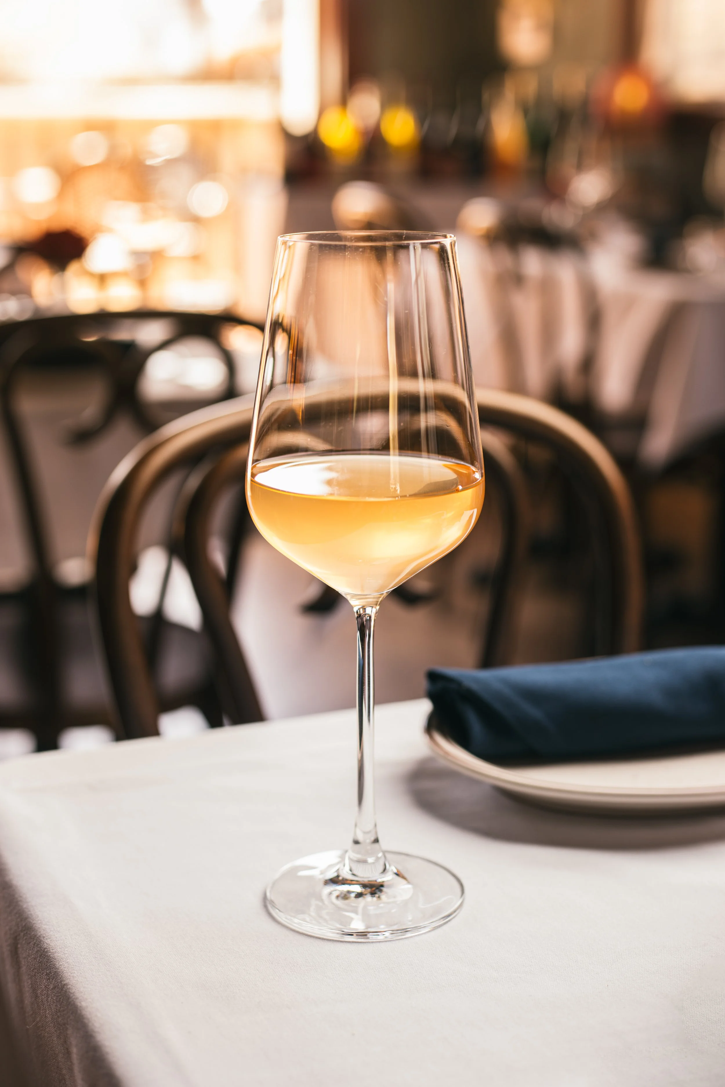 A glass of white wine on a table in a restaurant with blurred background.