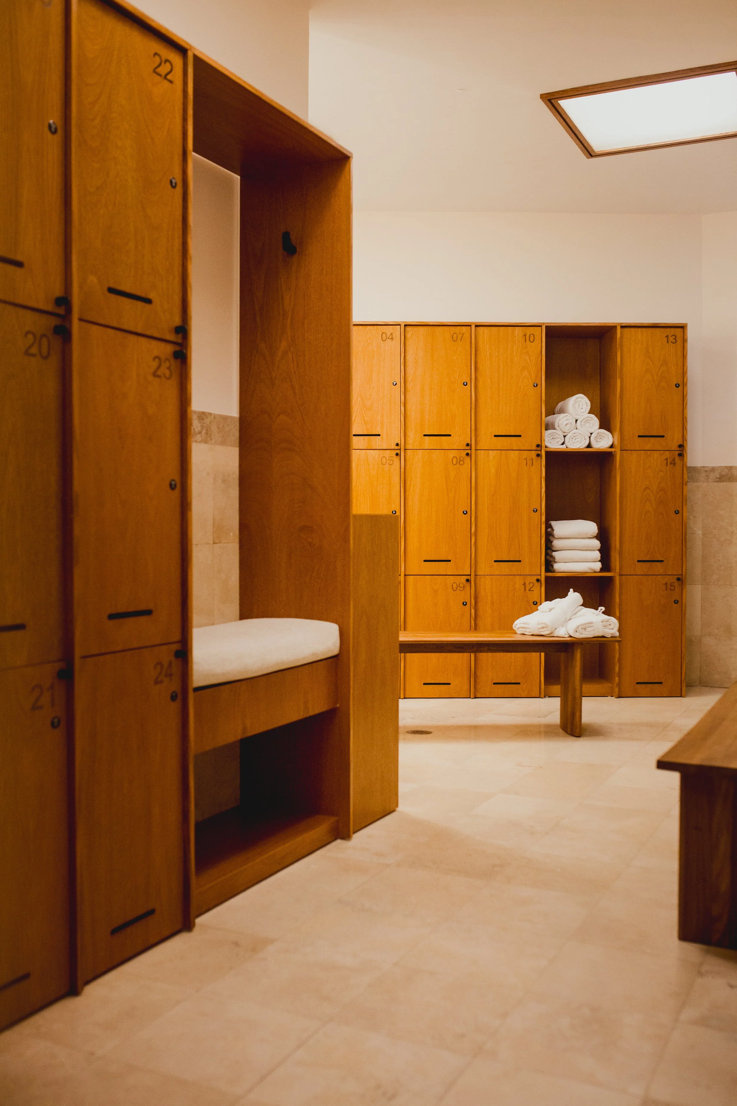 A locker room with wooden lockers, some of which contain rolled and folded white towels.