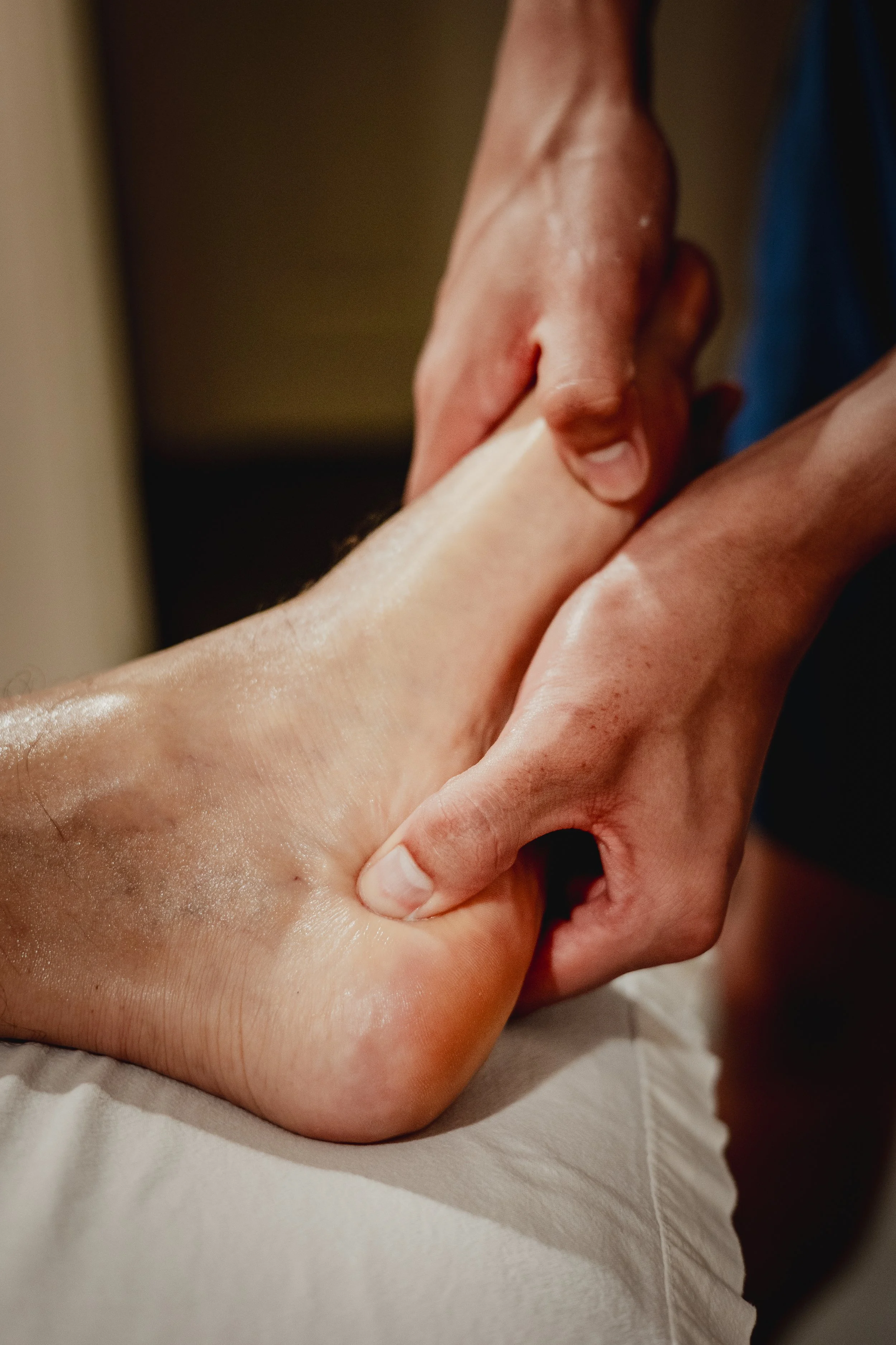 Close-up of a person receiving a massage, with hands applying pressure to their ankle and foot.