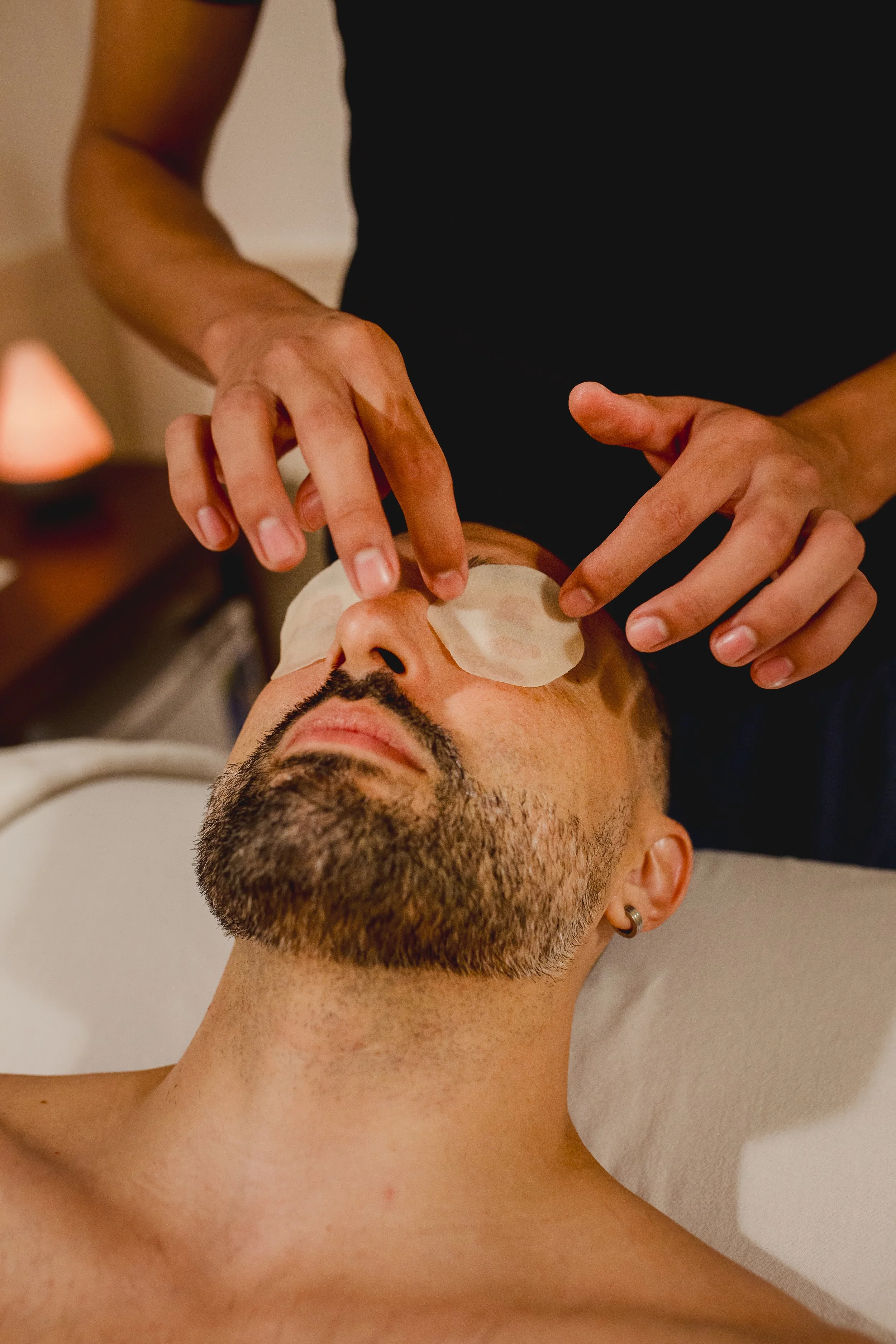 Man receives a facial treatment with eye patches while lying on a spa bed.