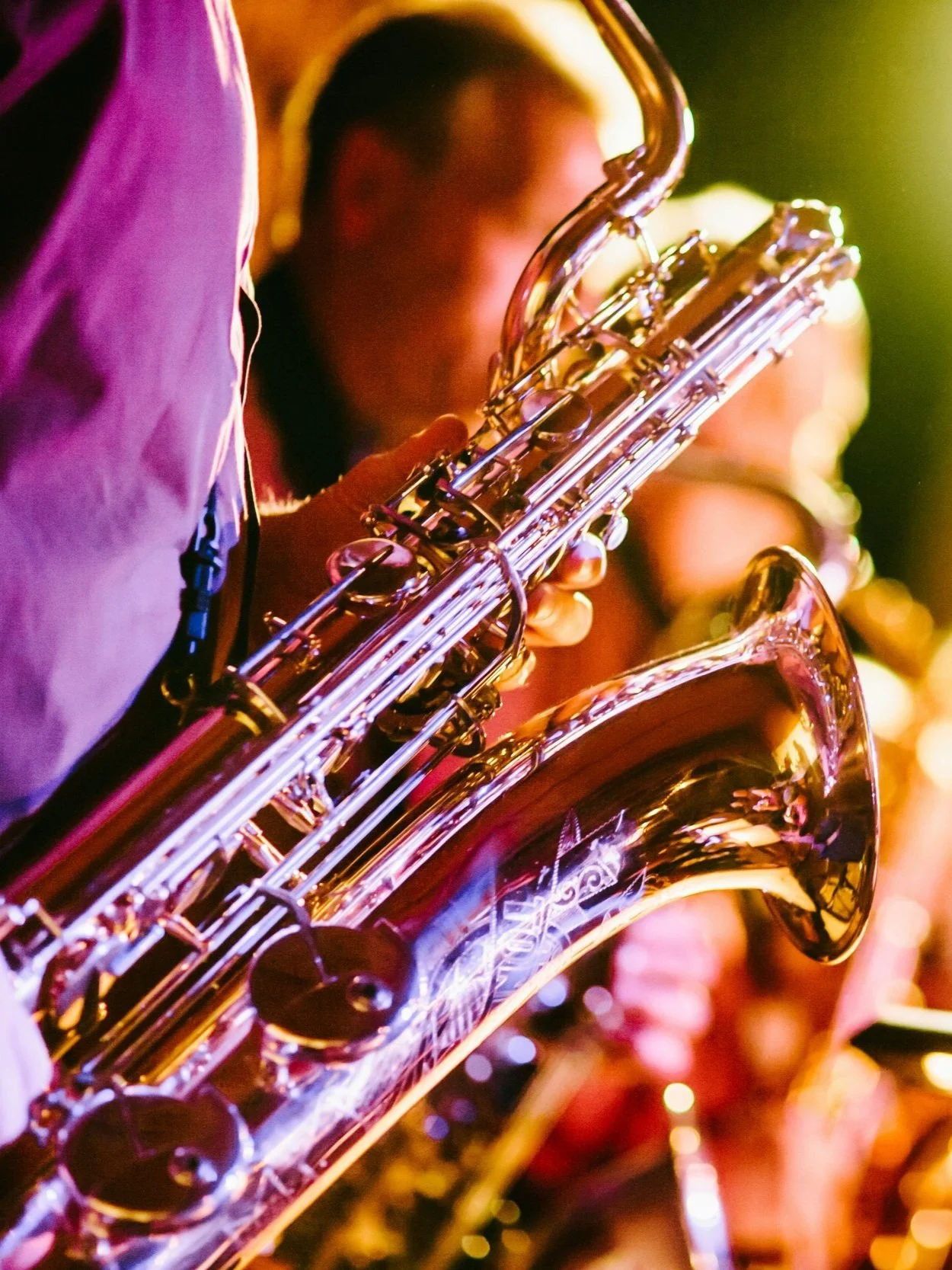 Close-up of a person playing a saxophone on stage with vibrant lighting.