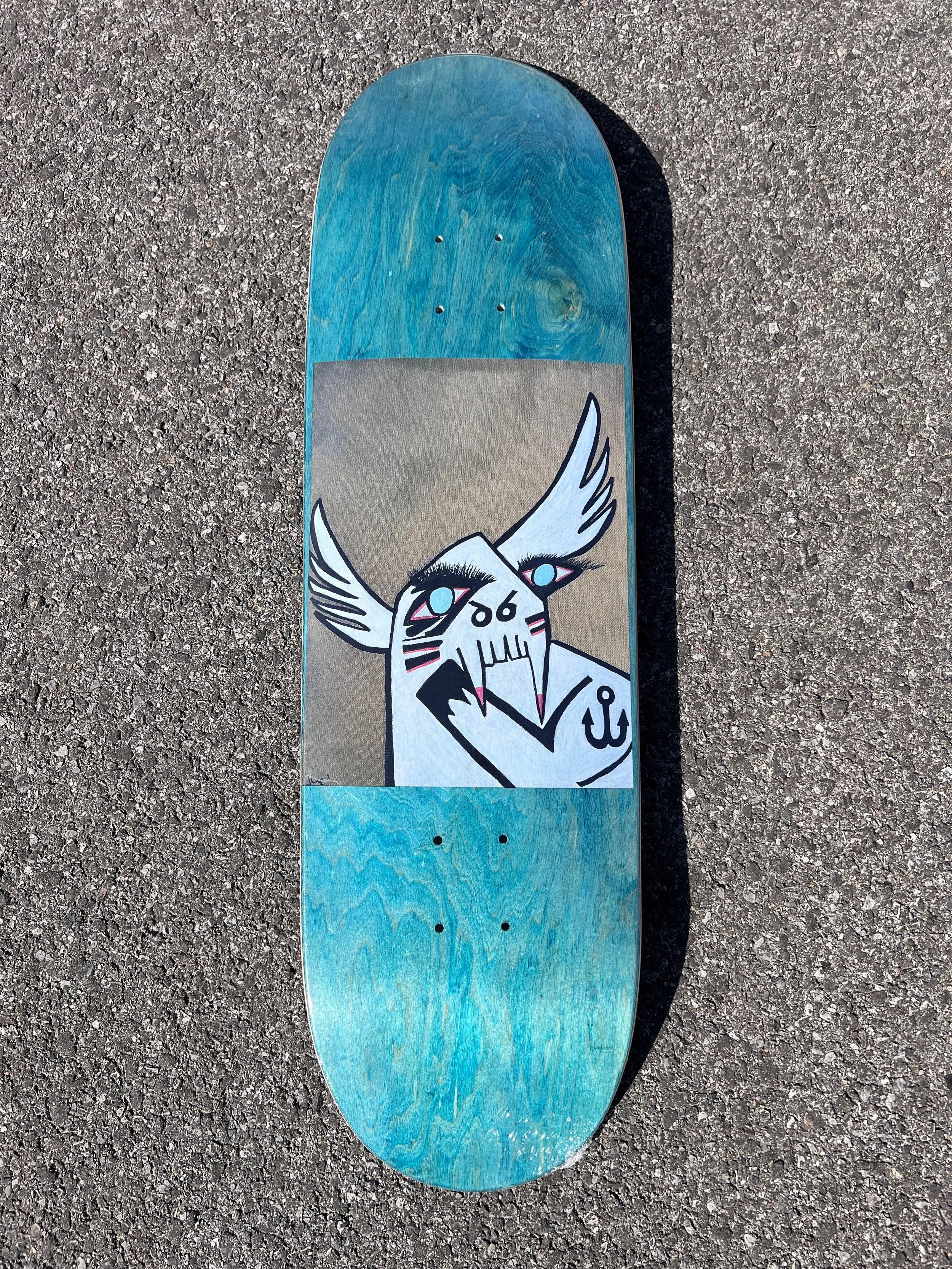 ArssiA- “Chief Buffalo Wing” Skateboard deck with a graphic of a stylized animal face, resembling a Buffalo, with wings on its head, in black, white, and pink, on a gold background, wood stain varies top and bottom.