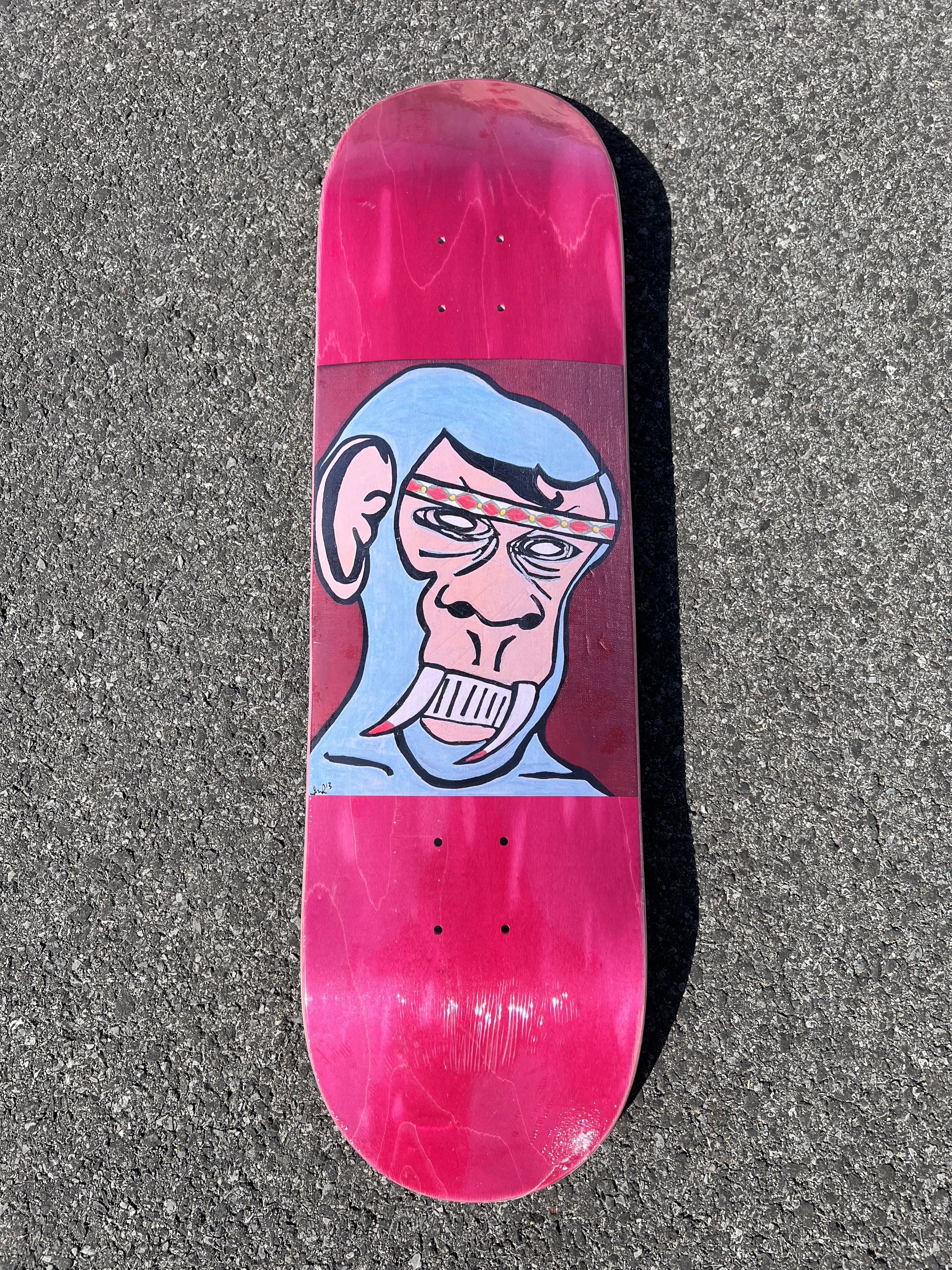 ArssiA- “Are we not all Animals?” Wood stain varies on a skateboard deck with a graffiti-style illustration of a monkey with blue fur, wrinkled face, wearing a headband, and baring teeth.