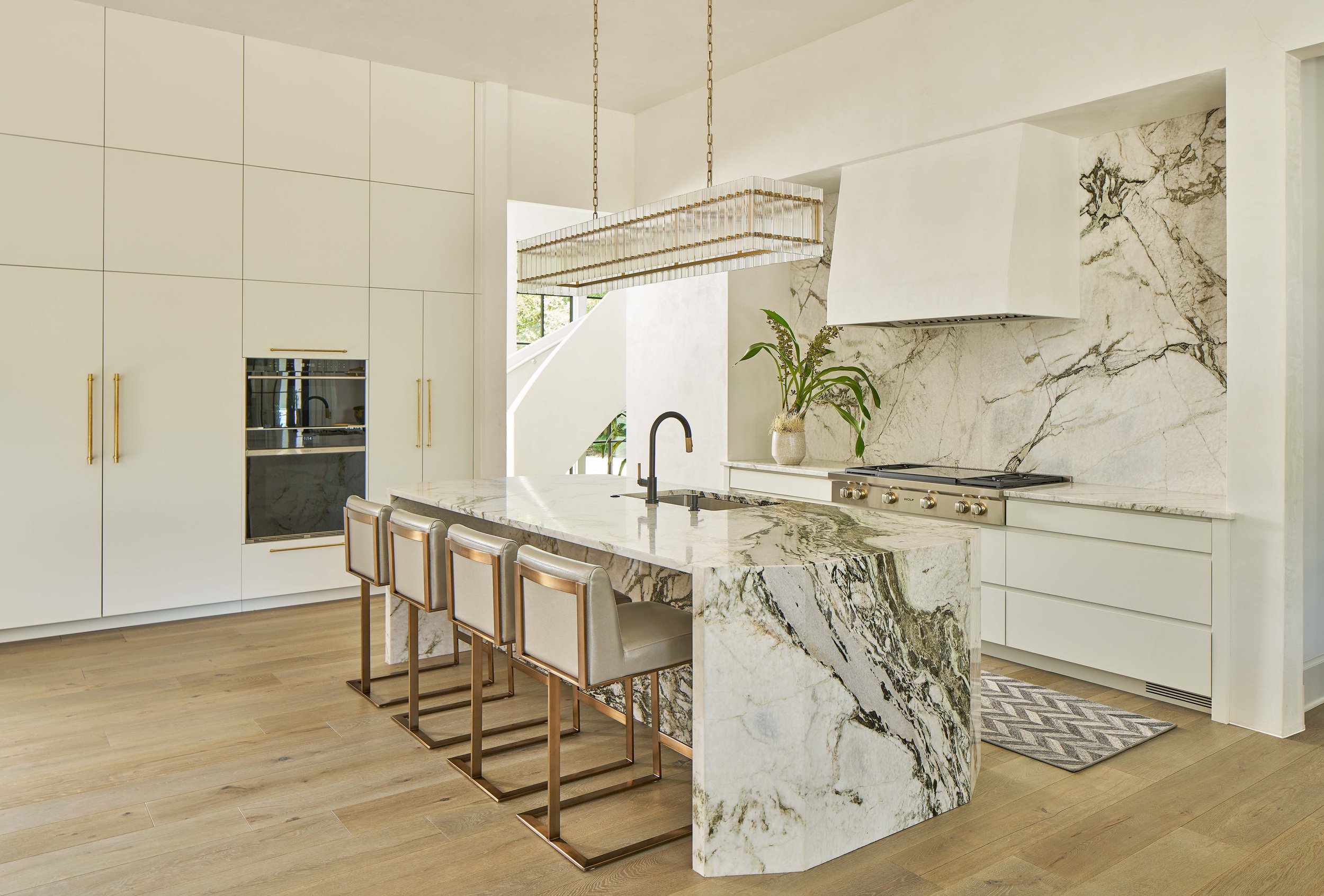 Modern kitchen with marble island, white cabinetry, and pendant lighting.