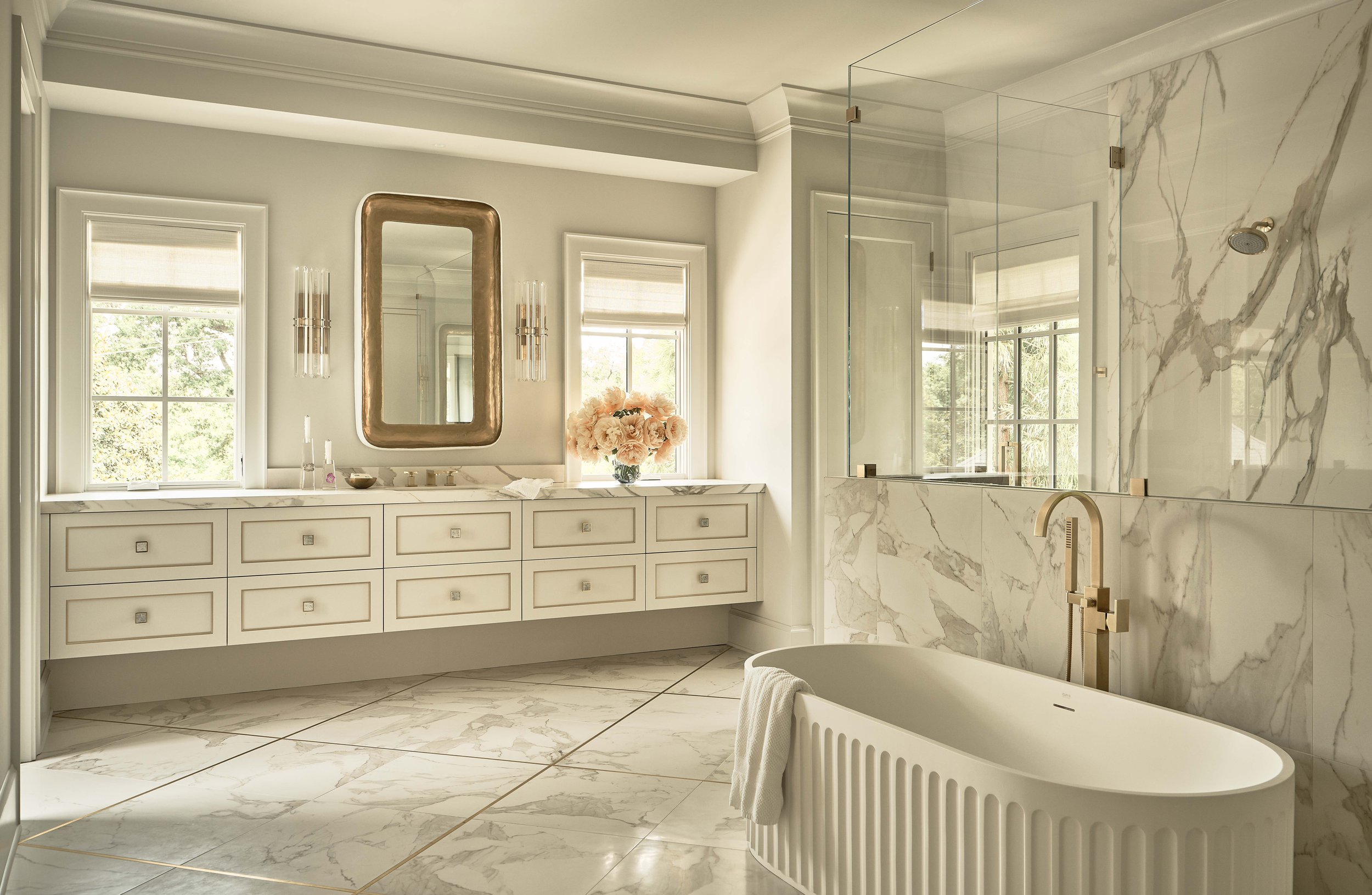 Elegant bathroom with freestanding bathtub, marble tiles, large mirror, dual sinks, and tall windows.