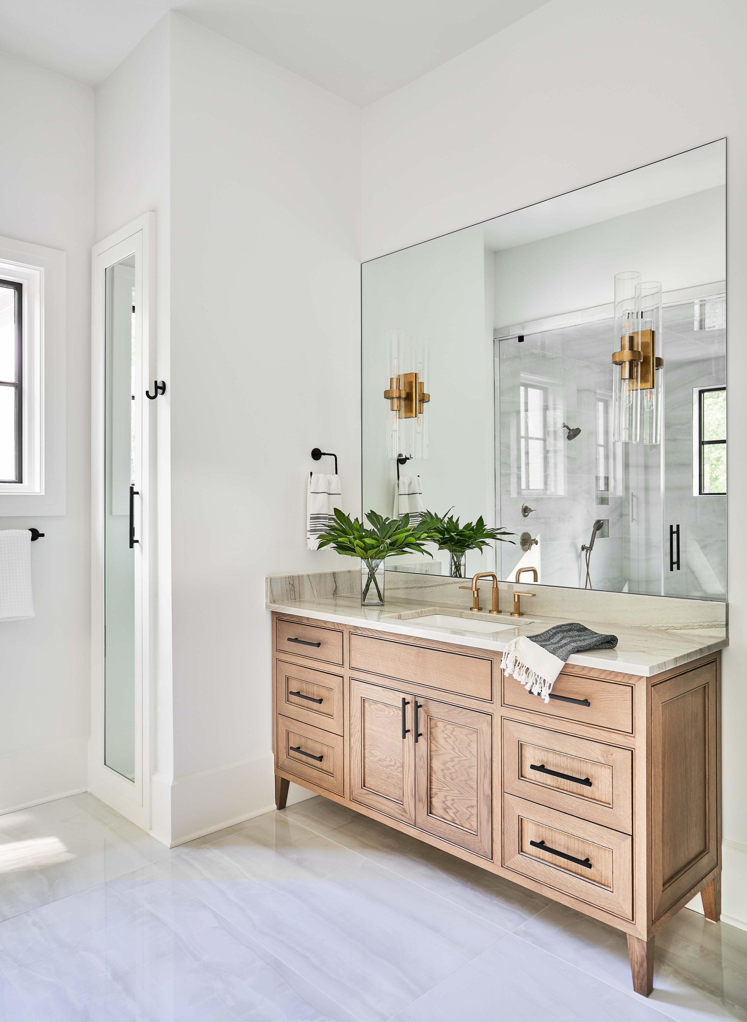 Modern bathroom with wooden vanity, marble countertop, large mirror, glass pendant lights, and green plant decoration.
