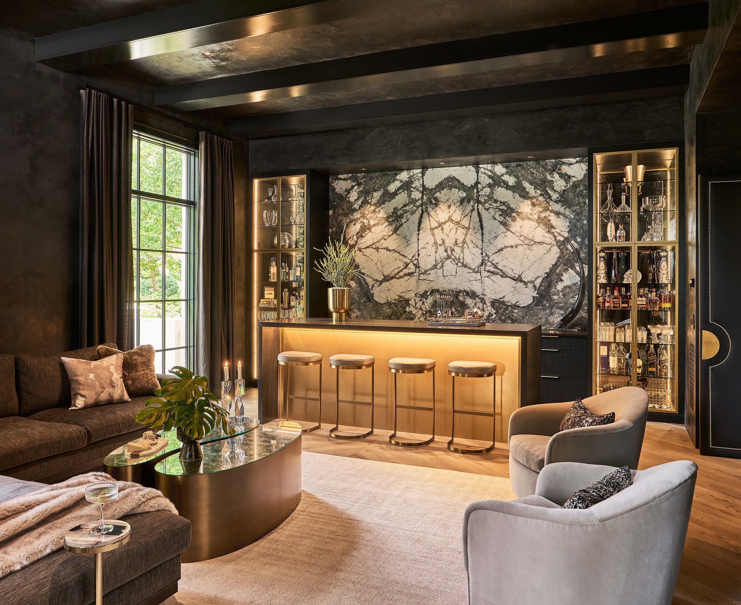 Modern luxurious bar and lounge area with dark walls, backlit marble bar, gold-trimmed bar stools, and plush furniture.