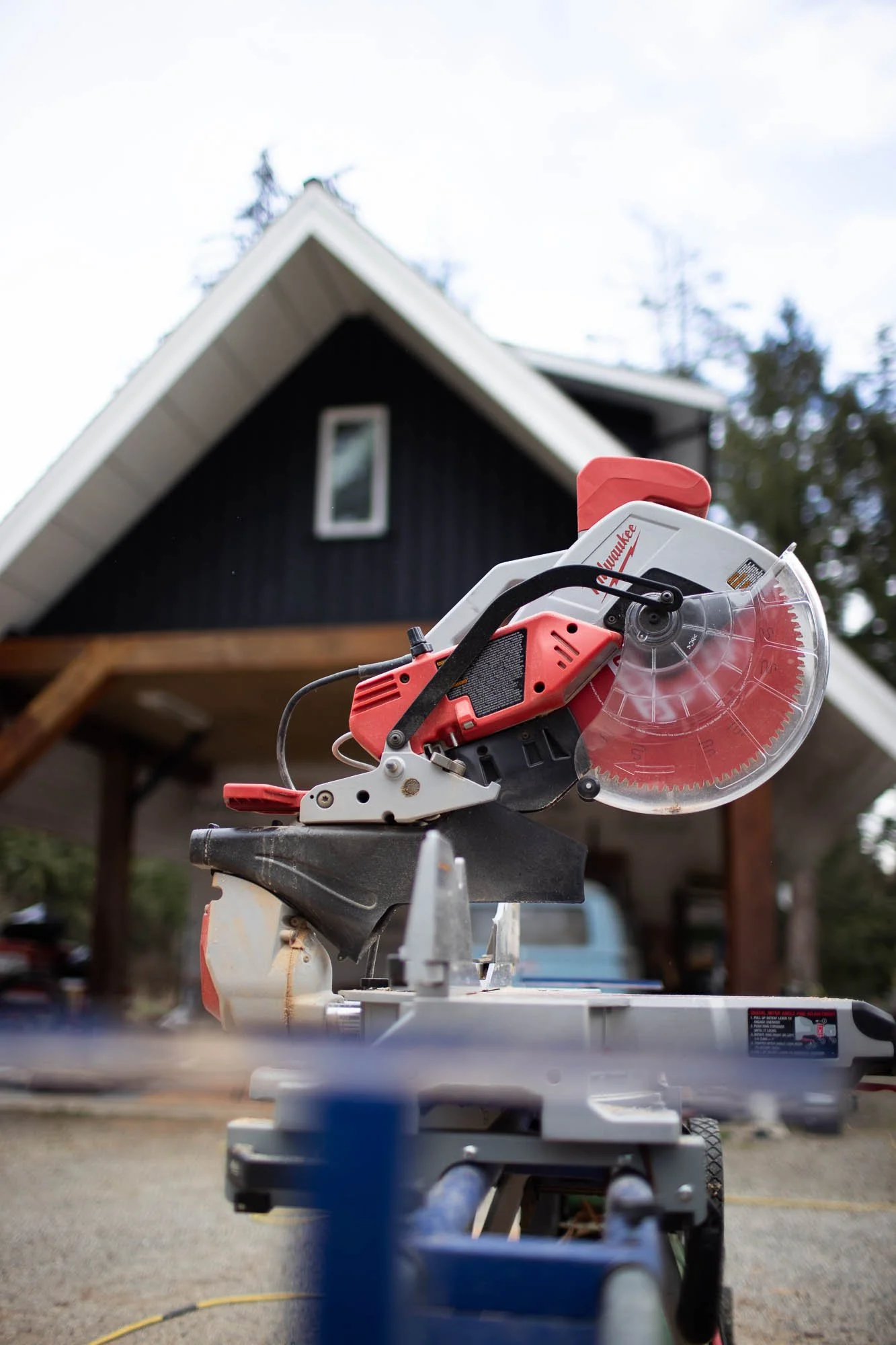 A miter saw positioned outdoors with a house and trees in the background.