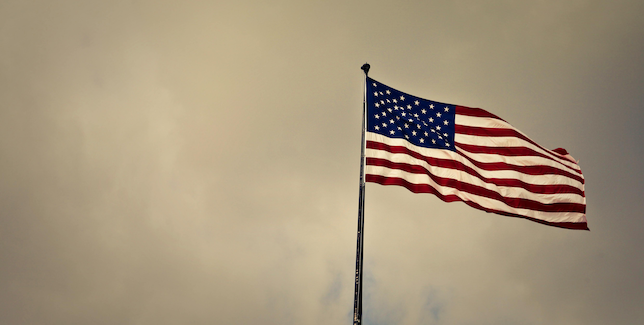 American flag waving on a flagpole against a cloudy sky.
