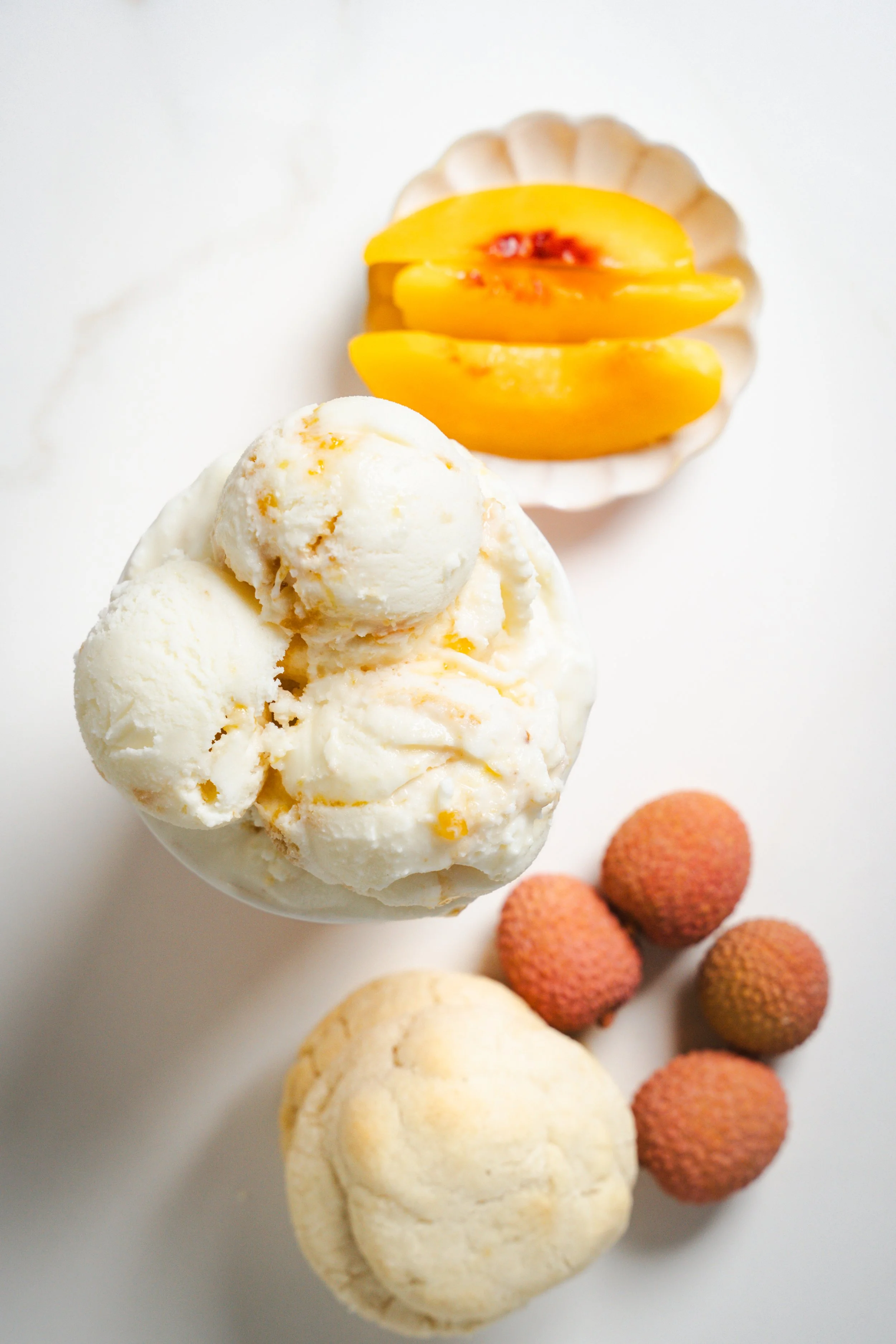 Peachy Lychee Sugar Cookie ice cream scoops, topped with peach slices and lychees on a white background.