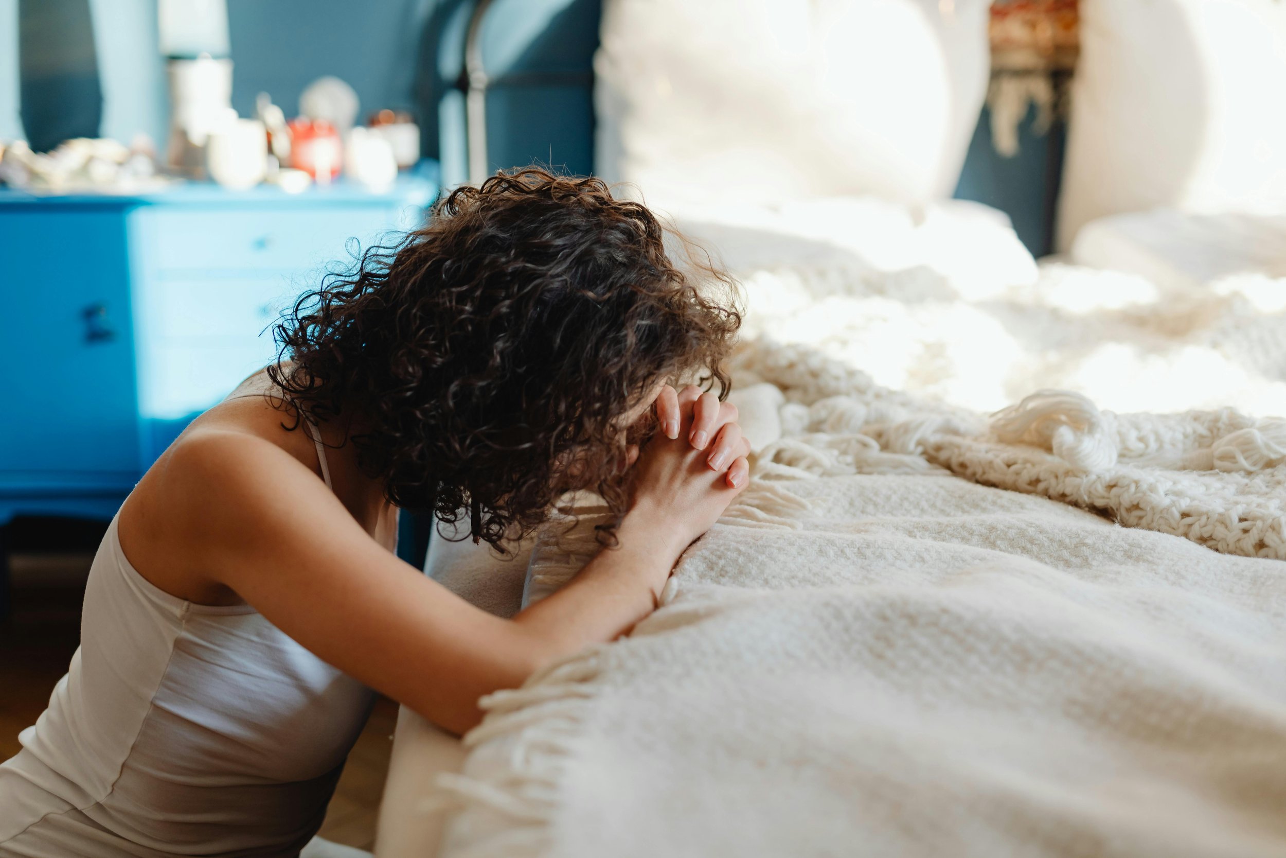Woman sitting on the edge of a bed with head in hands, reflecting anxiety, overthinking, and relationship overwhelm