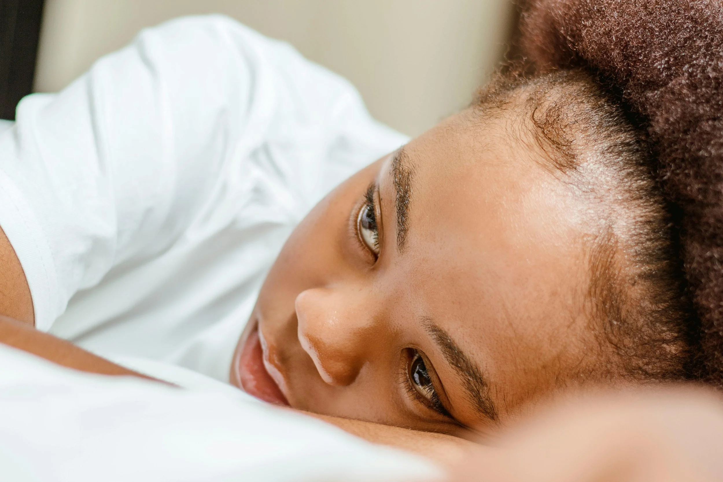 Black woman sitting alone looking emotionally overwhelmed and deep in thought, reflecting emotional sensitivity, overthinking, and relationship anxiety.
