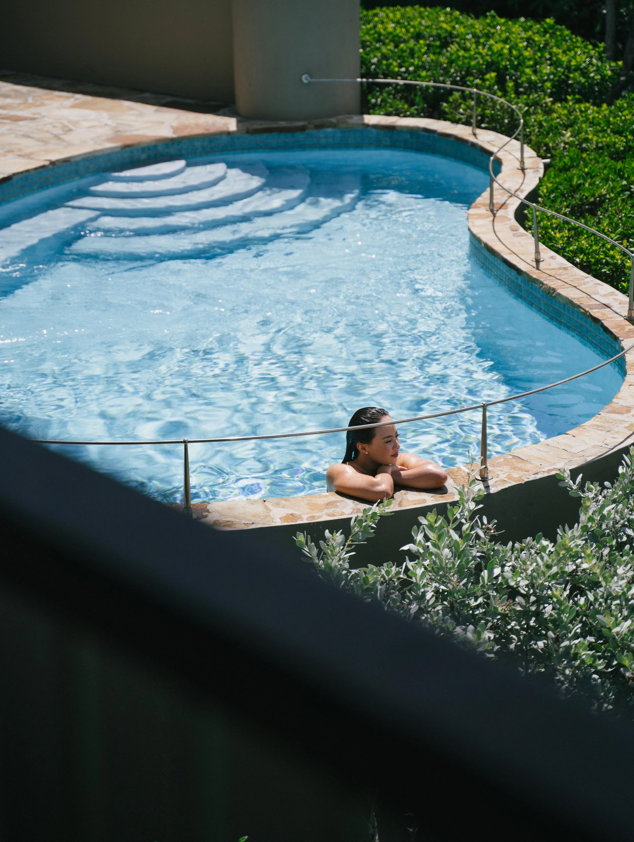 A woman relaxing in a swimming pool, leaning on the edge with her arms crossed.