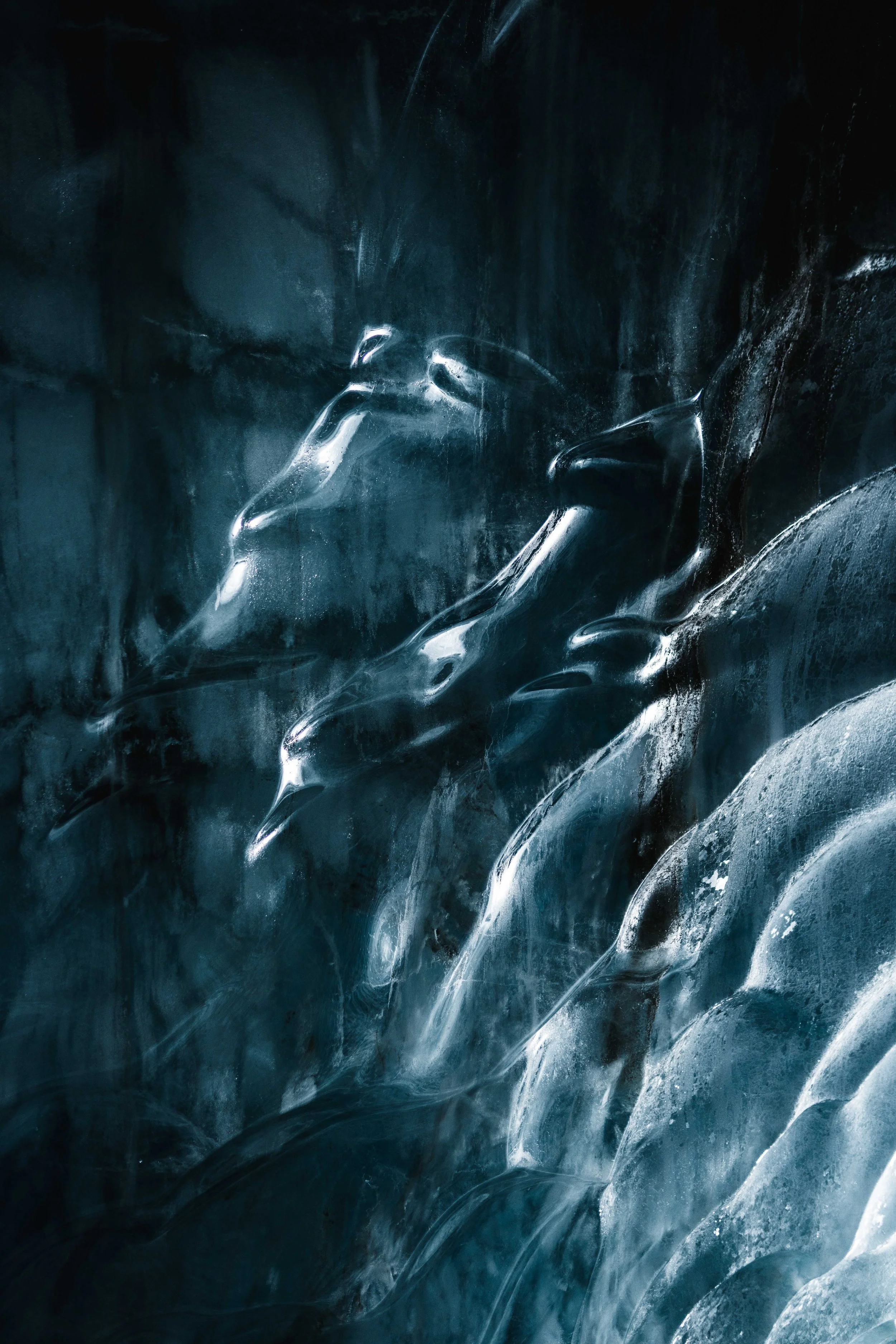 Close-up of ice with smooth, flowing shapes and reflective surfaces in shades of blue and black.