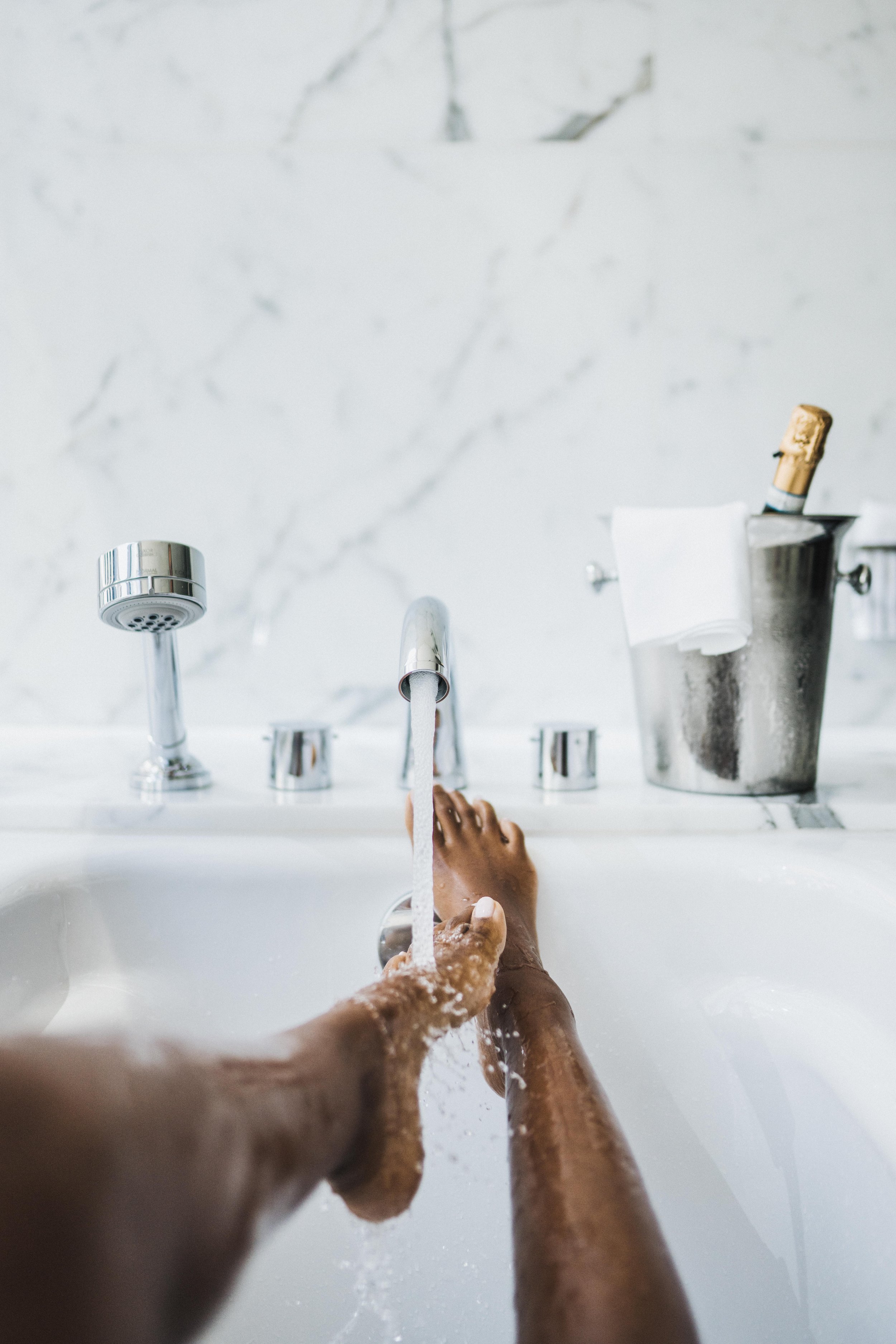 A person washing their feet in a bathtub with running water.