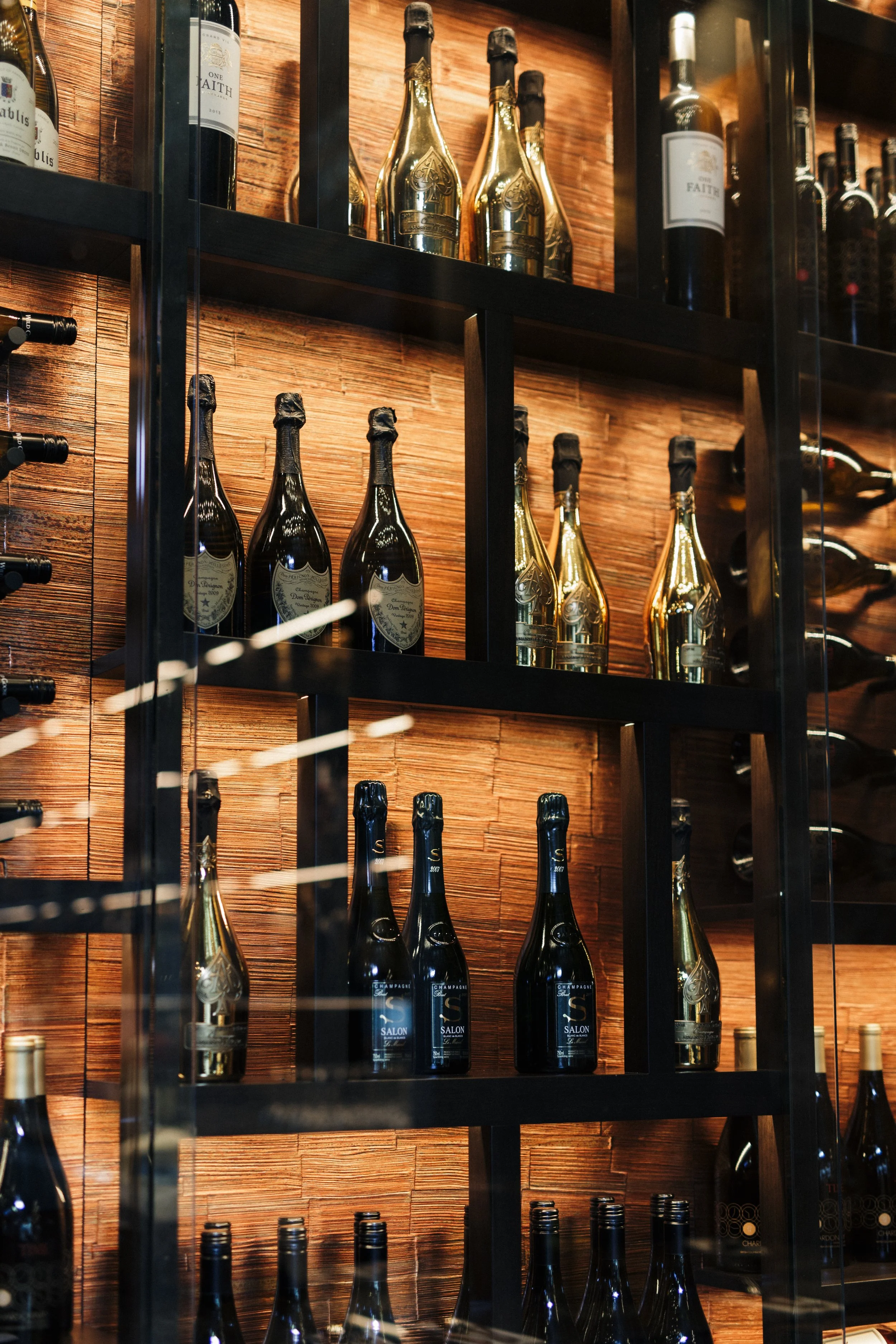 A wine display with shelves holding various bottles of champagne and wine, set against a wooden wall with a black metal frame.
