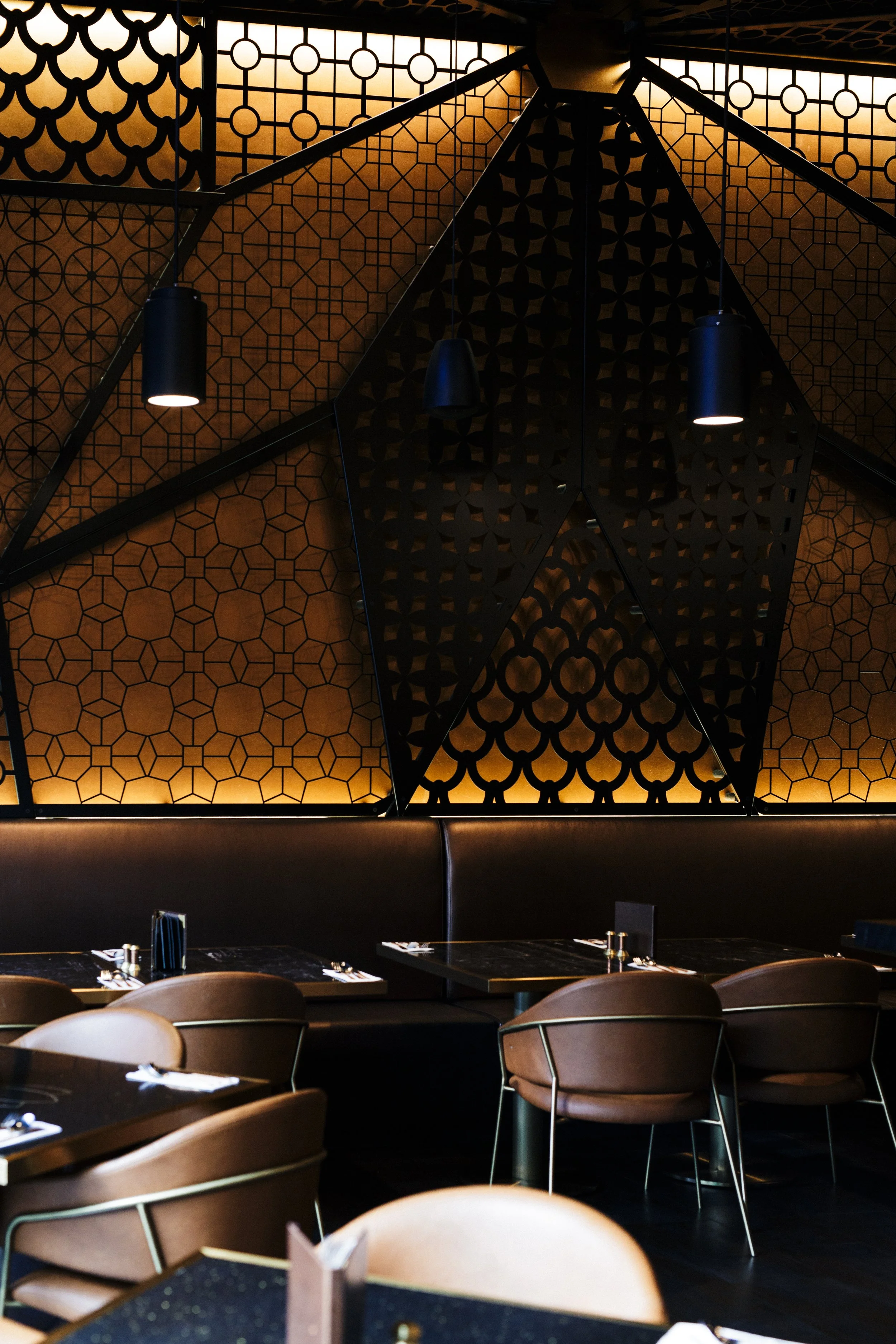 Elegant restaurant interior with black geometric decorative wall panels, warm lighting, and brown chairs around black tables.