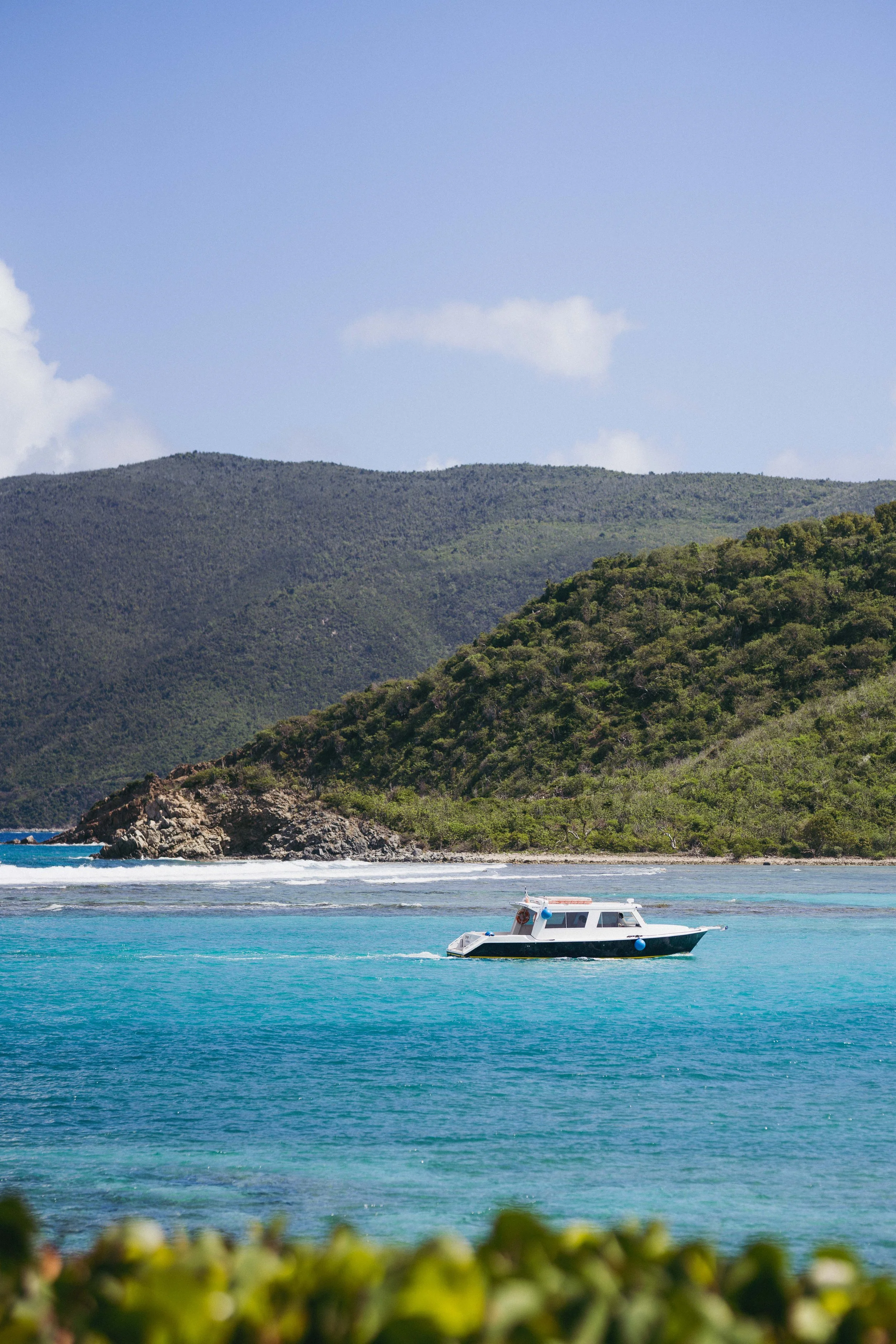 A boat sailing on blue water near a green coastline with hills in the background.
