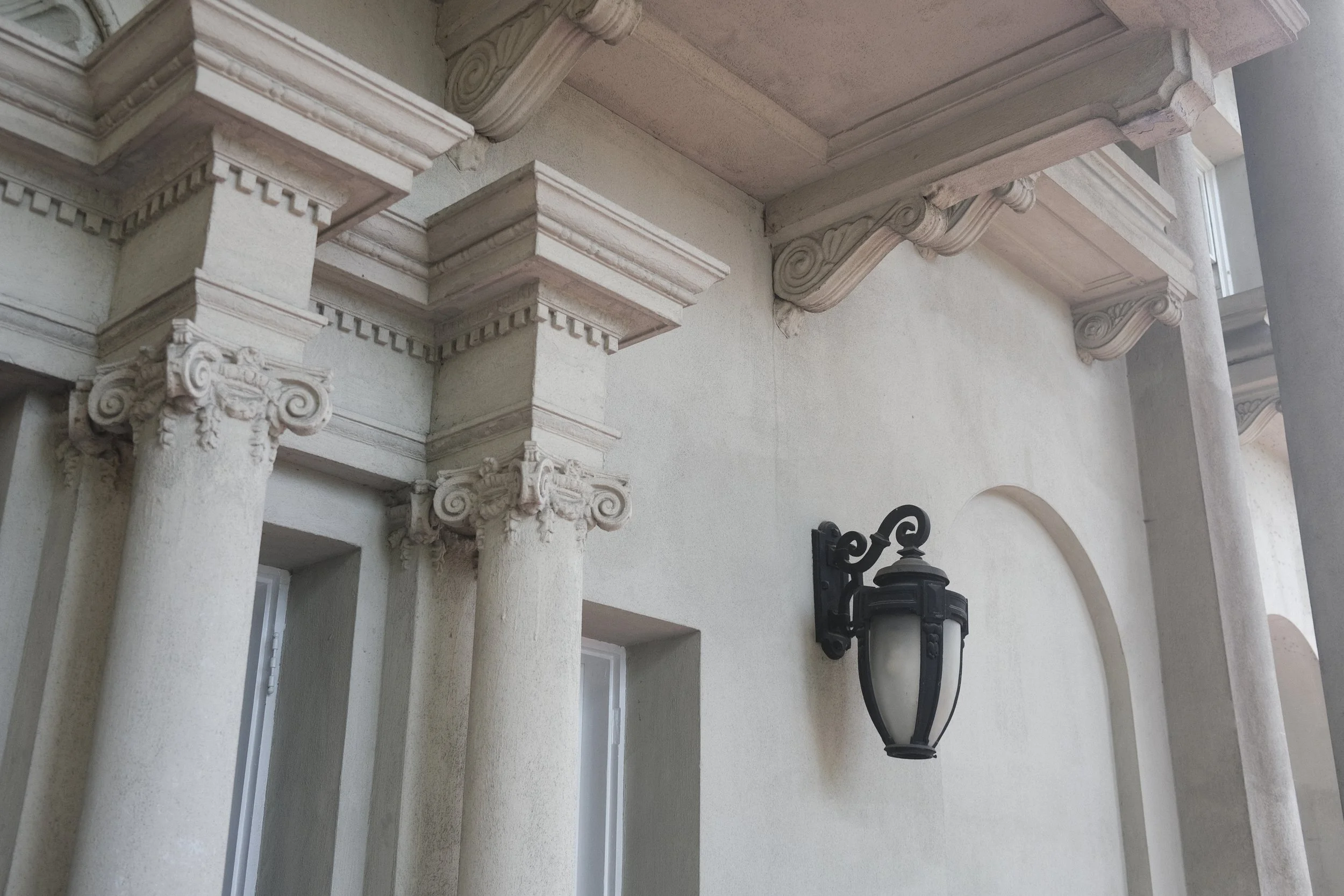 Close-up of a classic architectural exterior with ornate white columns, decorative crown molding, and a black wall-mounted lantern.