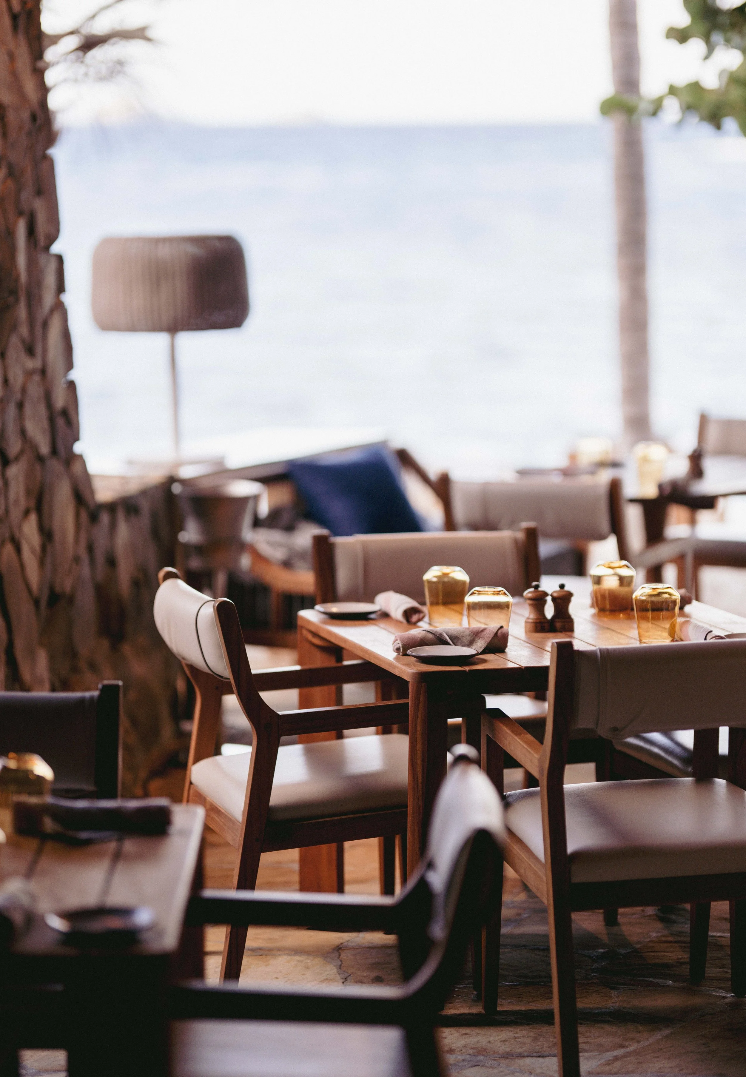 Dining area overlooking the water with wooden tables, chairs, and decorative table settings.