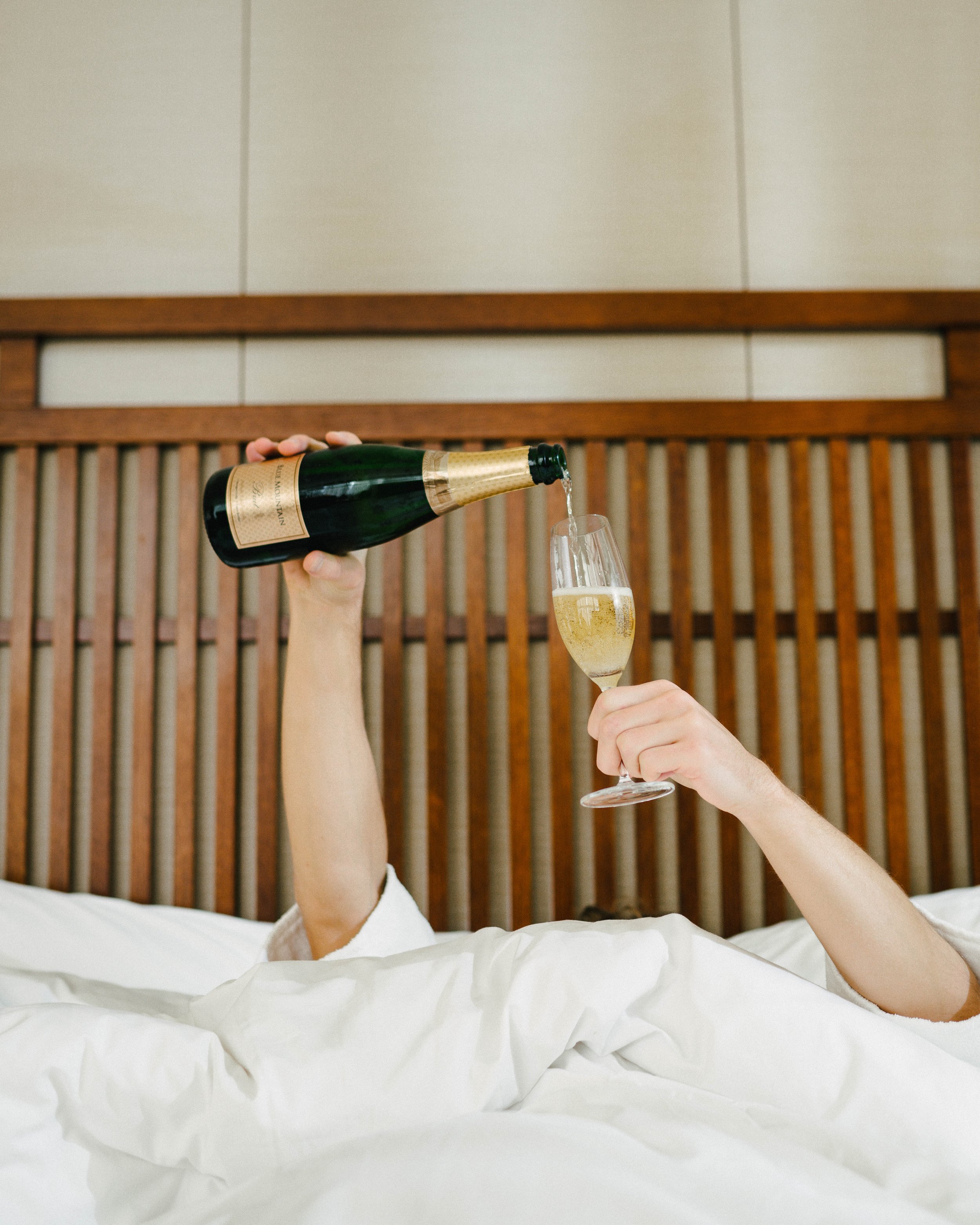 Person in bed pouring champagne into a glass.