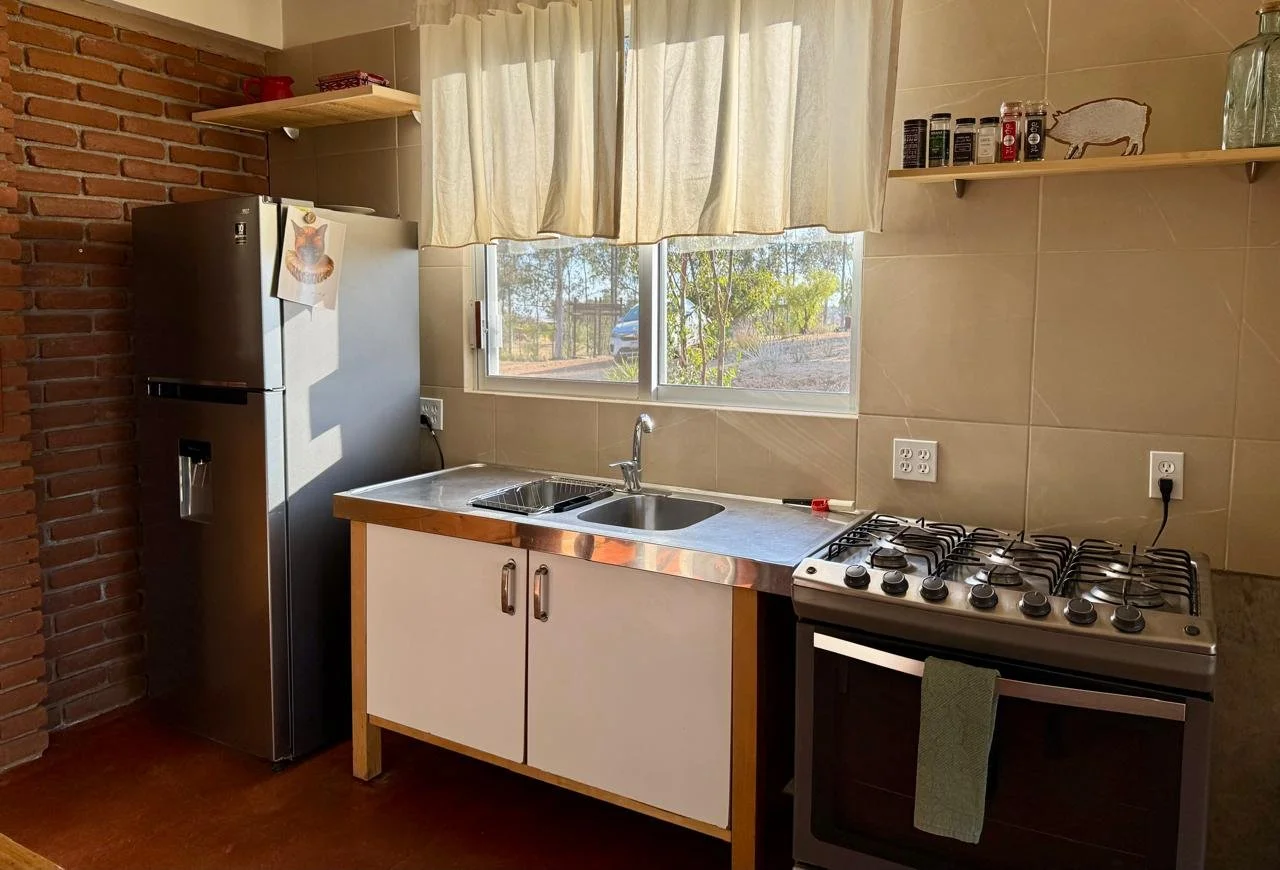 Cocina con refrigerador, fregadero, estufa y ventana con cortinas. Decoración sencilla