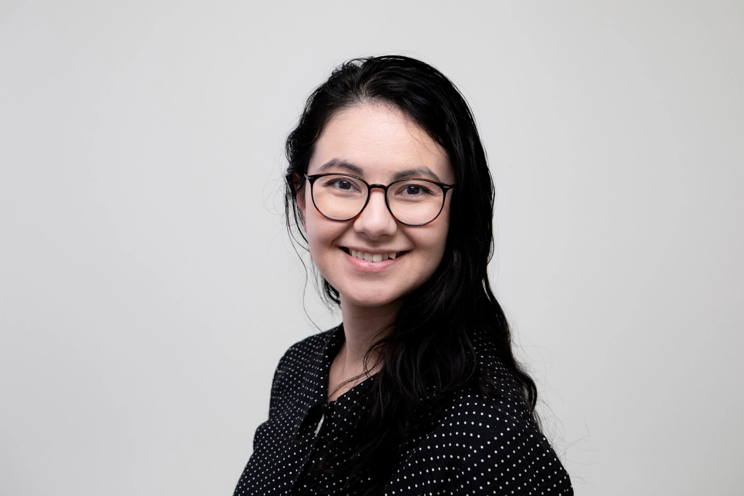 Portrait of dark haired woman with glasses smiling.