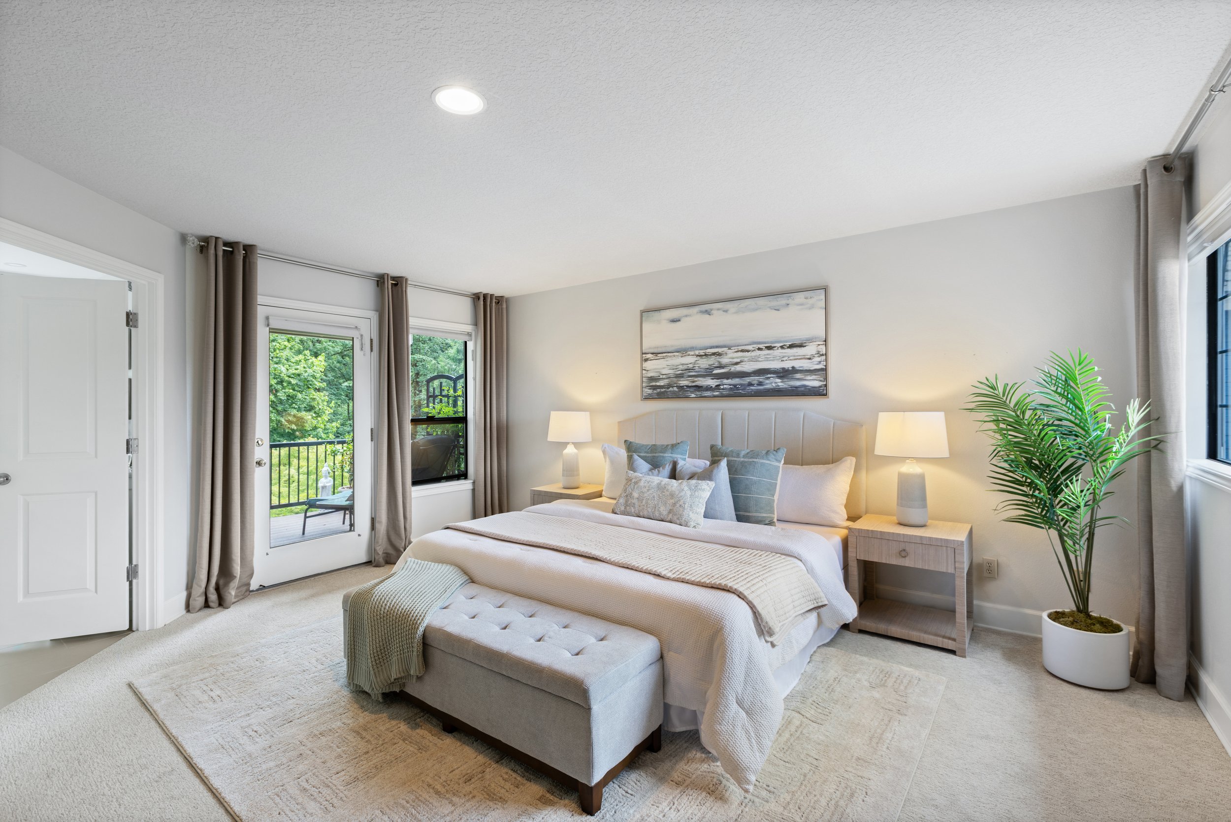 Bright bedroom with a large bed, nightstands with lamps, a painting above the bed, and a potted plant near the window.