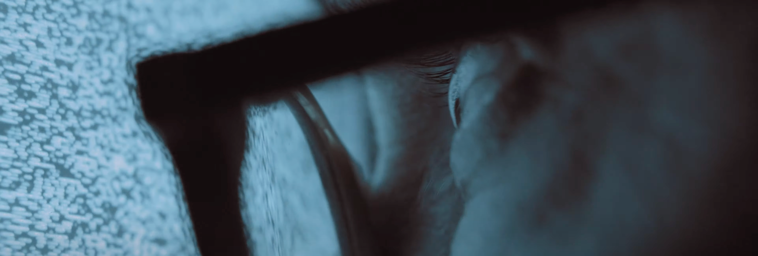 A close-up of a person wearing glasses, with their eye visible and a finger touching the glasses.