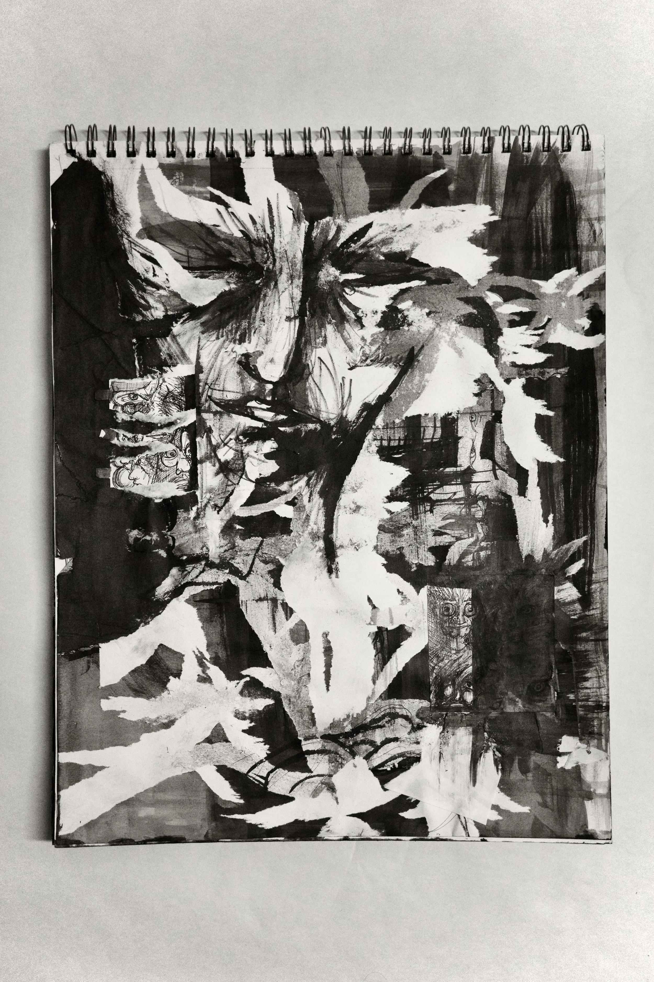 Black and white abstract art on a spiral-bound sketchbook with a portrait of a person's face and hand, with expressive brush strokes and artistic sketches.