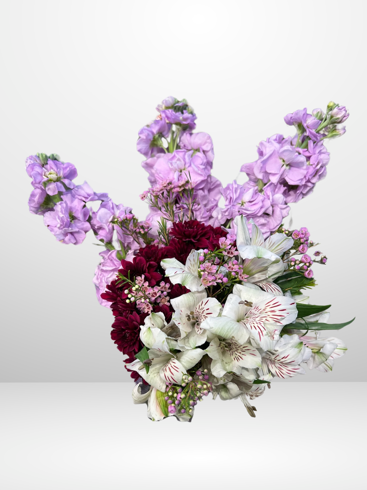 Floral arrangement with purple, maroon, and white flowers against a plain background.