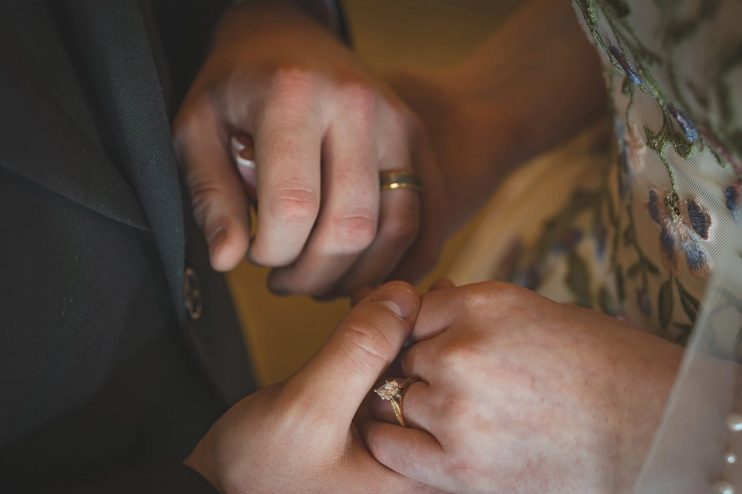 Close-up of a couple exchanging rings, with one person's hand placing an engagement ring onto the other's finger.