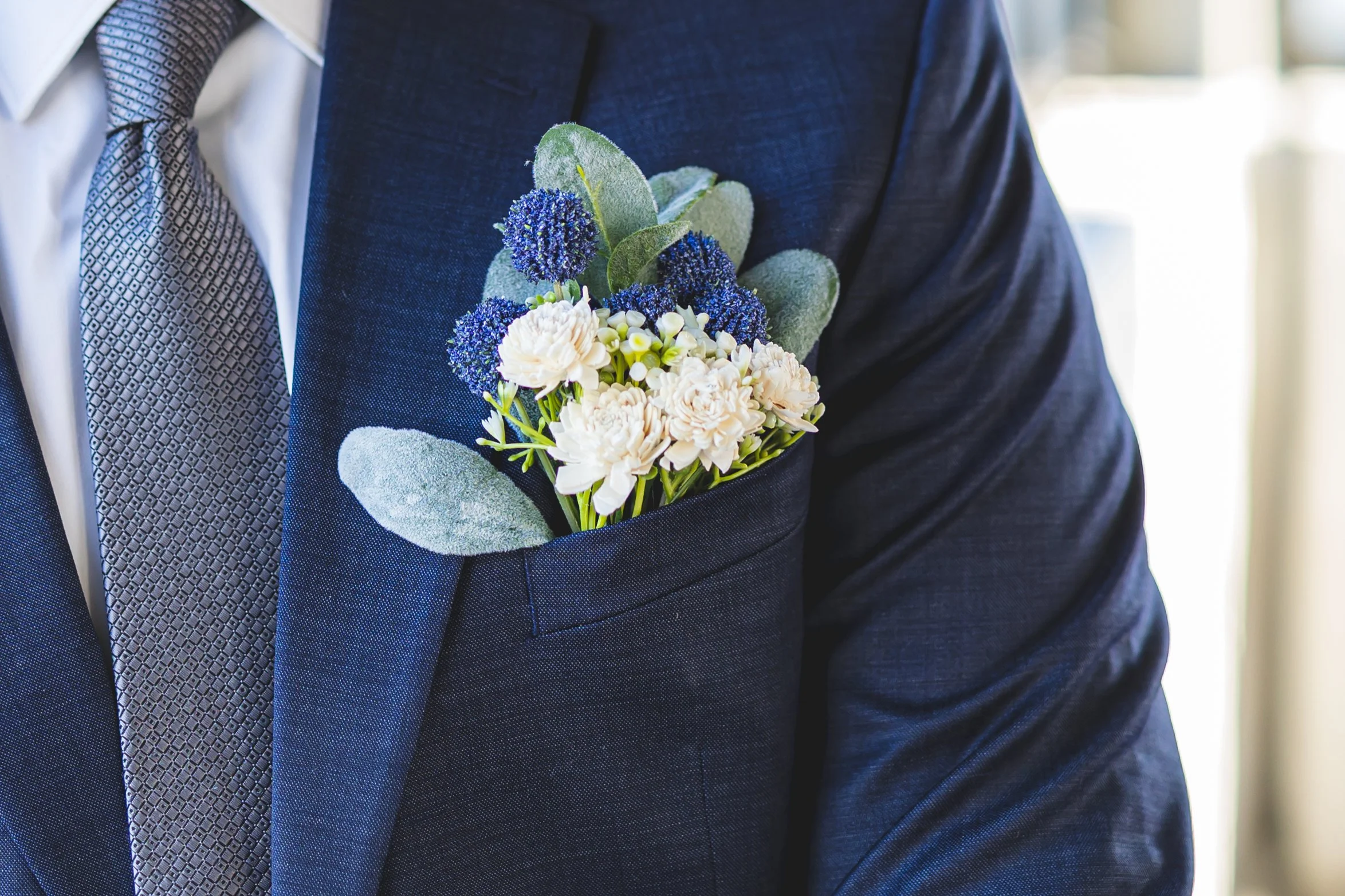 A man in a dark blue suit with a boutonniere of white and blue flowers, including carnations and statice, pinned to his chest.
