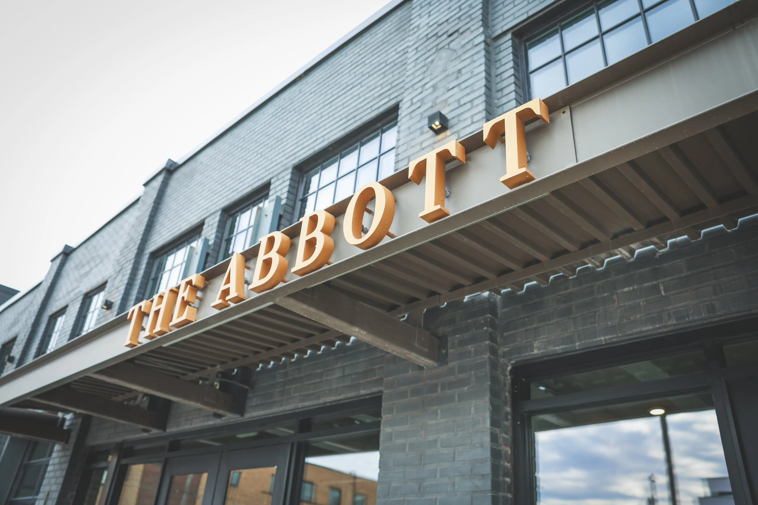 Sign reading "THE ABBOTT" on the exterior of a modern building with brick walls and large windows. 