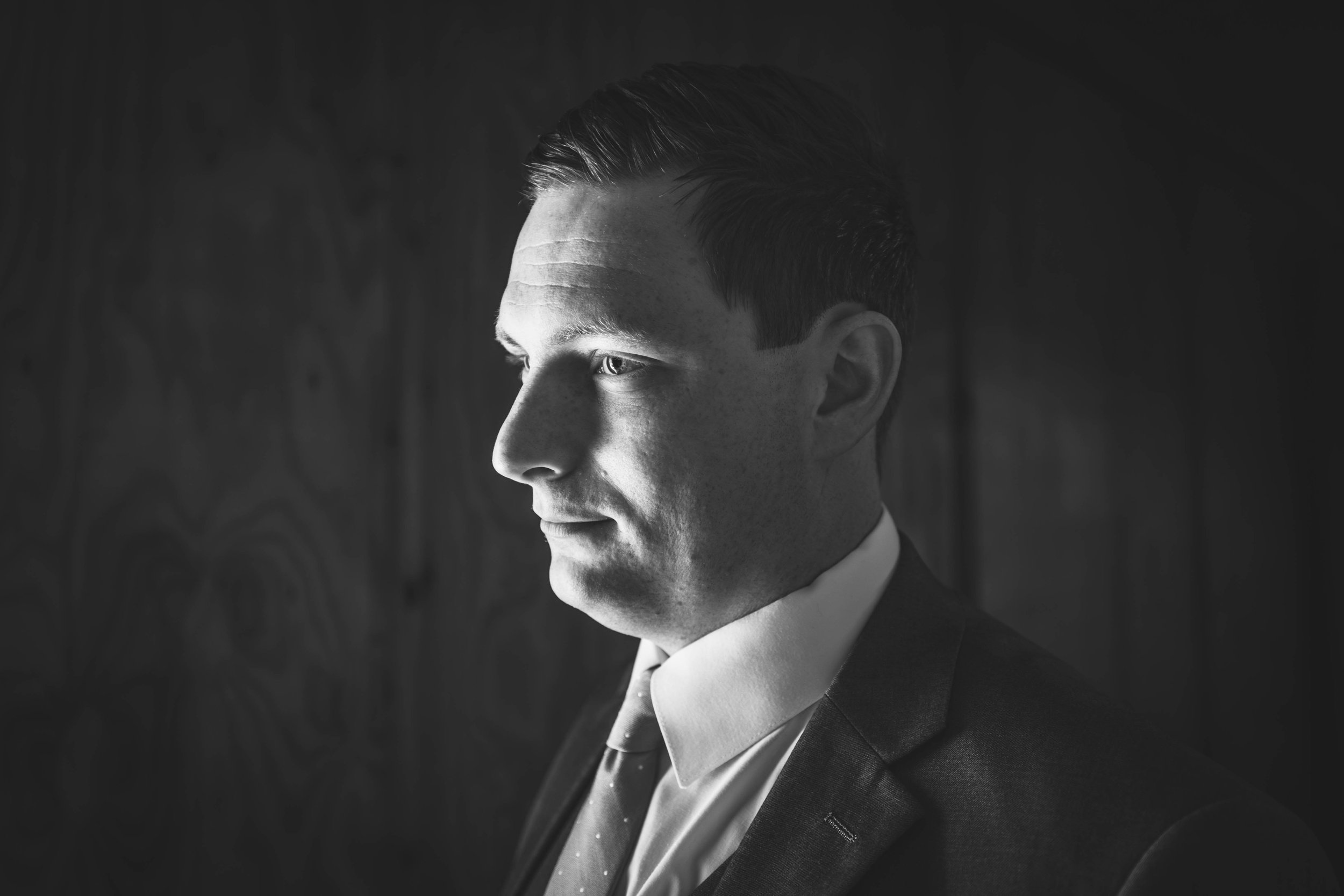 Black and white photo of a young man with styled hair, dressed in a suit, looking to the side with a serious expression.