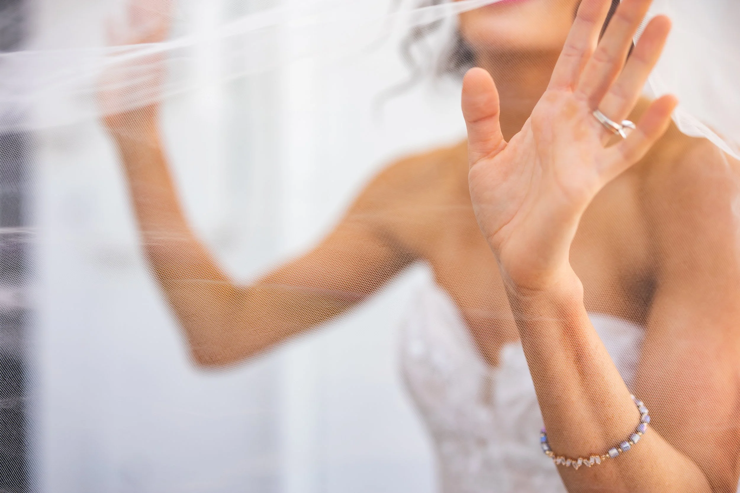 Woman behind a semi-transparent fabric, touching it with her hand, wearing a ring and a beaded bracelet.