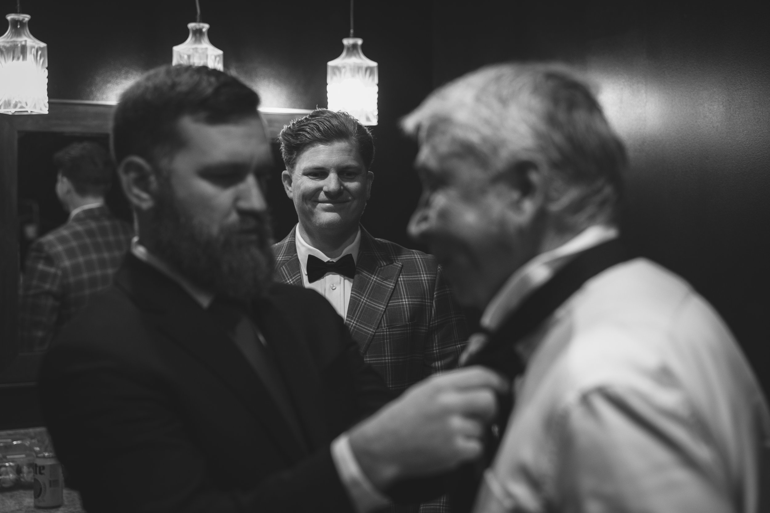 Three men in tuxedos, one with a beard, another with gray hair, and a third with a smile, in a black-and-white photo at a formal event.