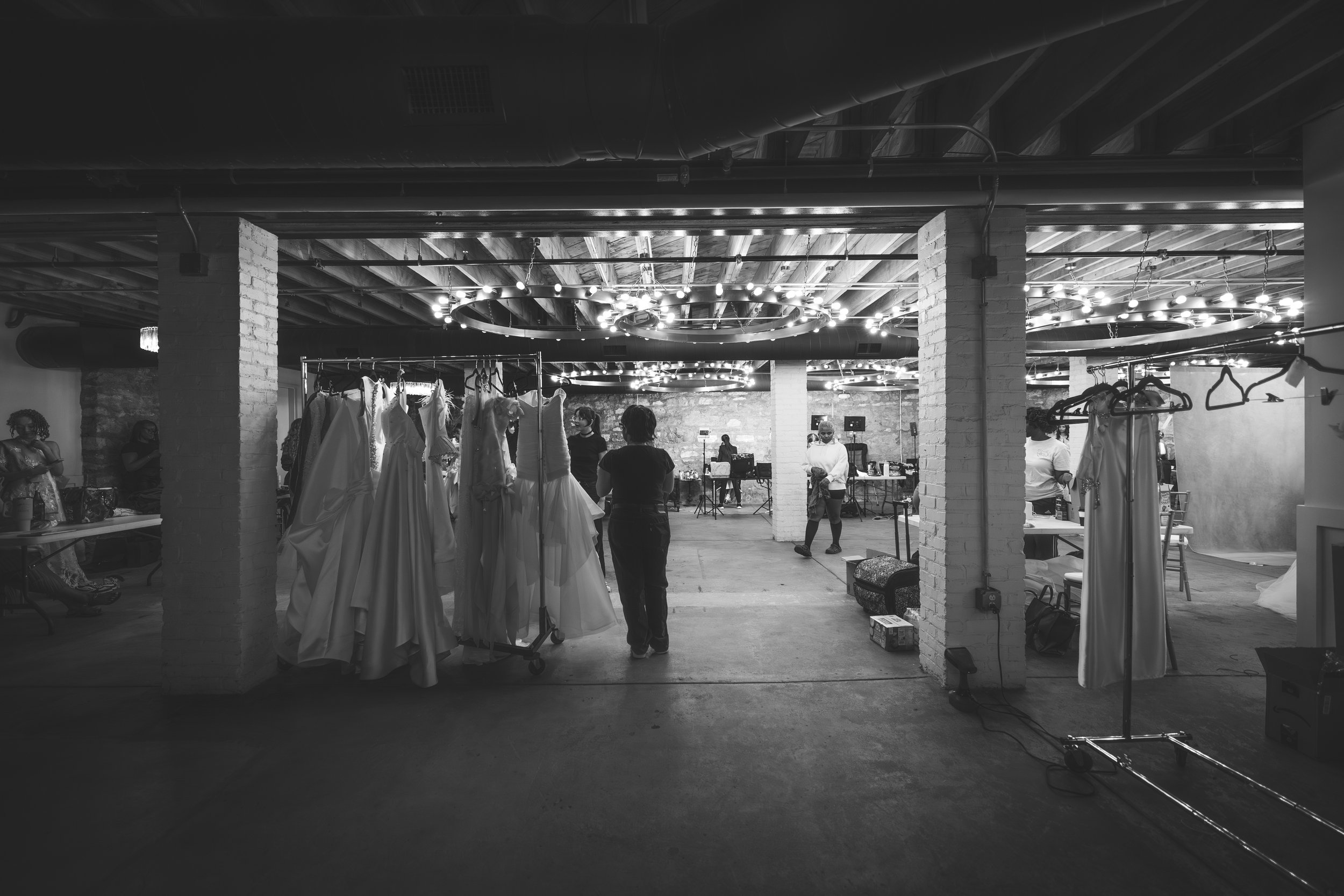 Interior of a creative space with white brick pillars, hanging lights, and clothing racks with dresses, possibly a costume or dress shop.
