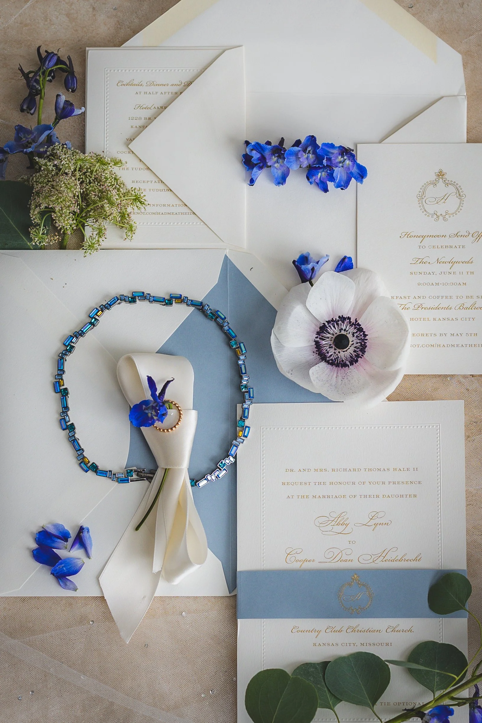 Wedding invitation suite with blue and white flower accents, jewelry, and decorative elements on a flat surface.