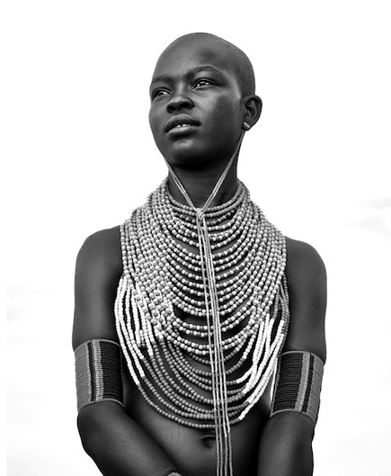 A young person wearing multiple strands of beaded necklaces and arm accessories, posed against a plain background.