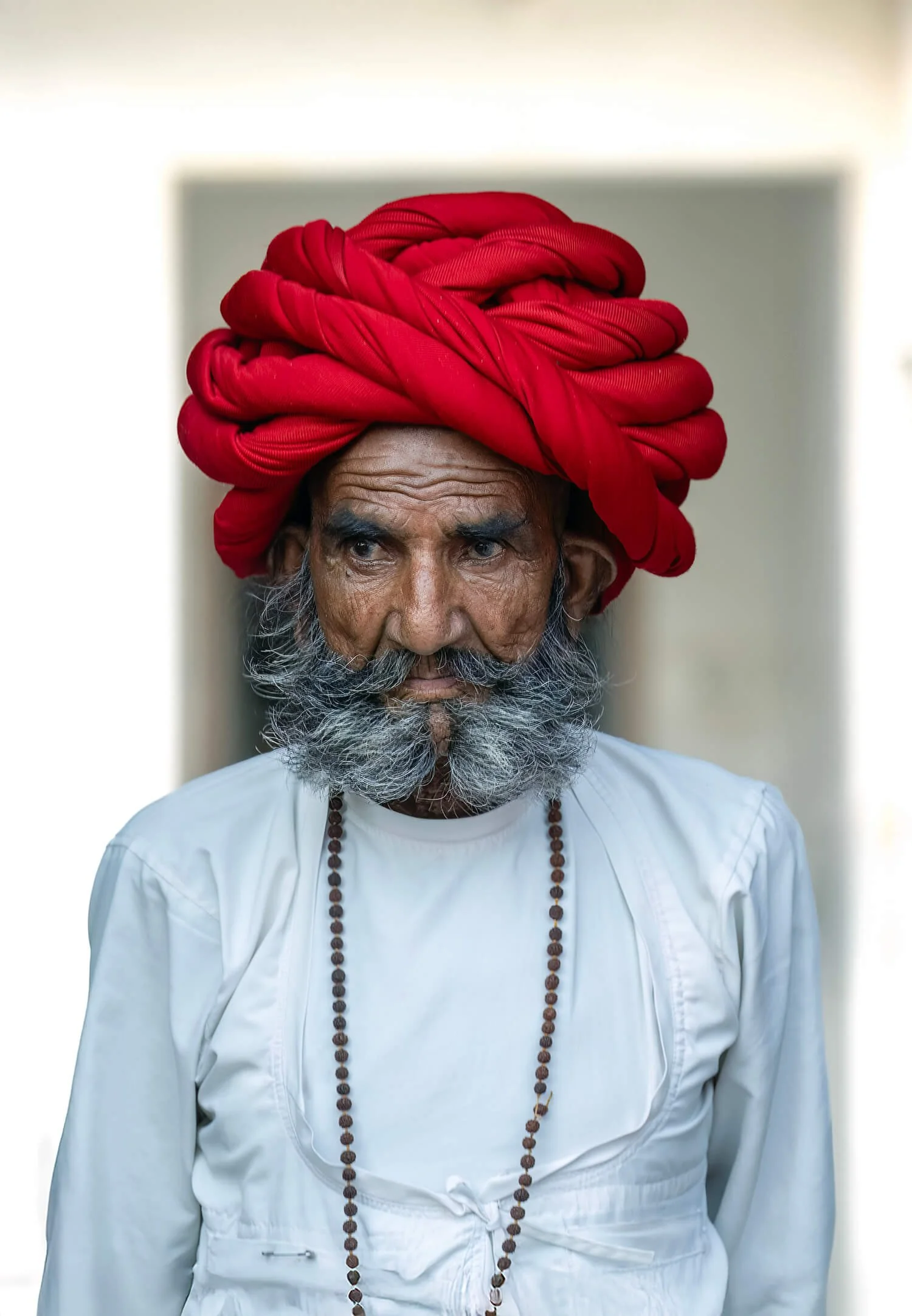 A Rabiri herdsman wearing traditional clothing consisting of a large red turban, a white shirt, and a beaded necklace.  He was just leaving his home.  Photographed in Jawai, India.