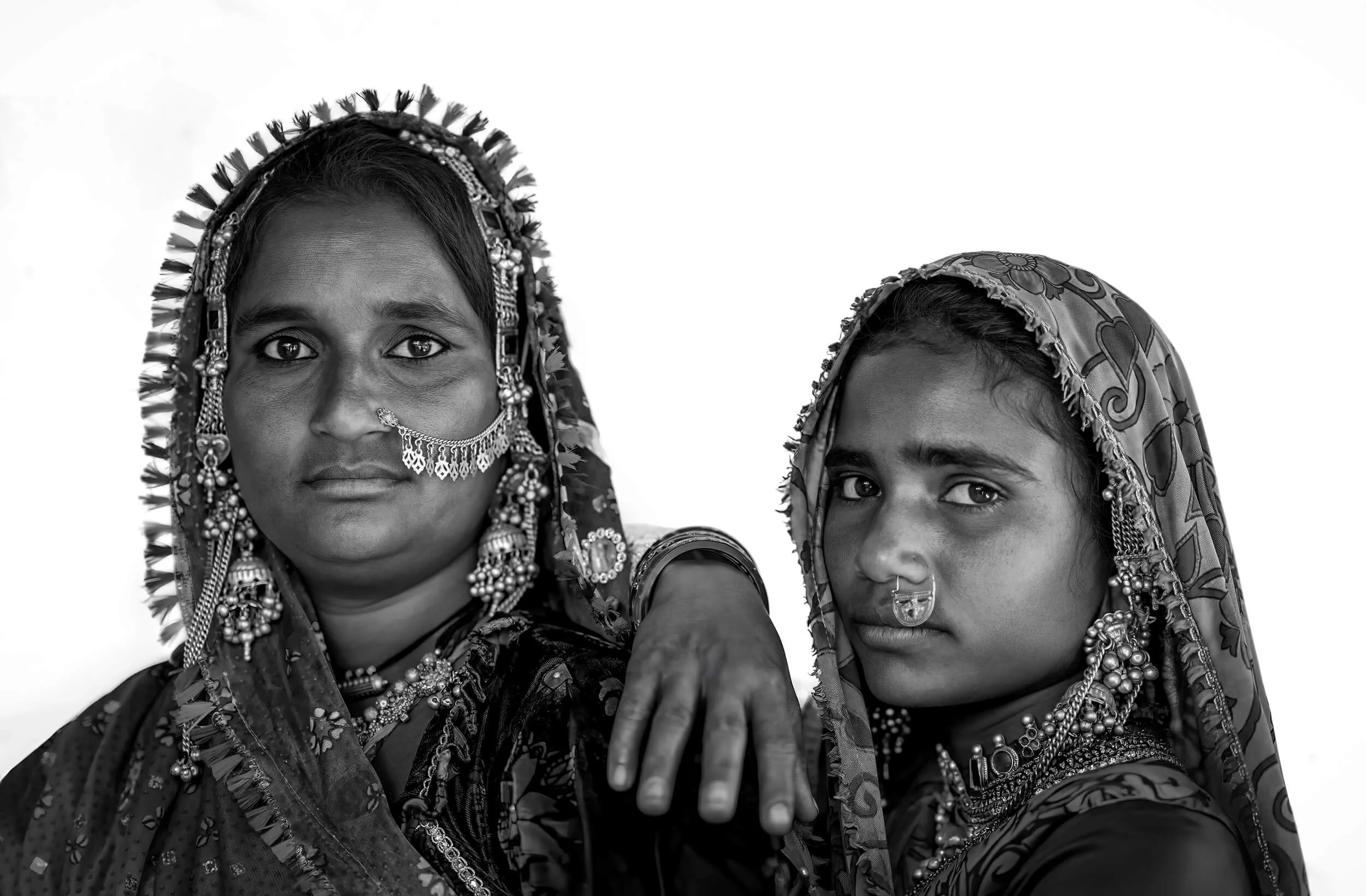 Two women wearing traditional Indian clothing and jewelry, with scarves covering their heads, posing closely together in black and white