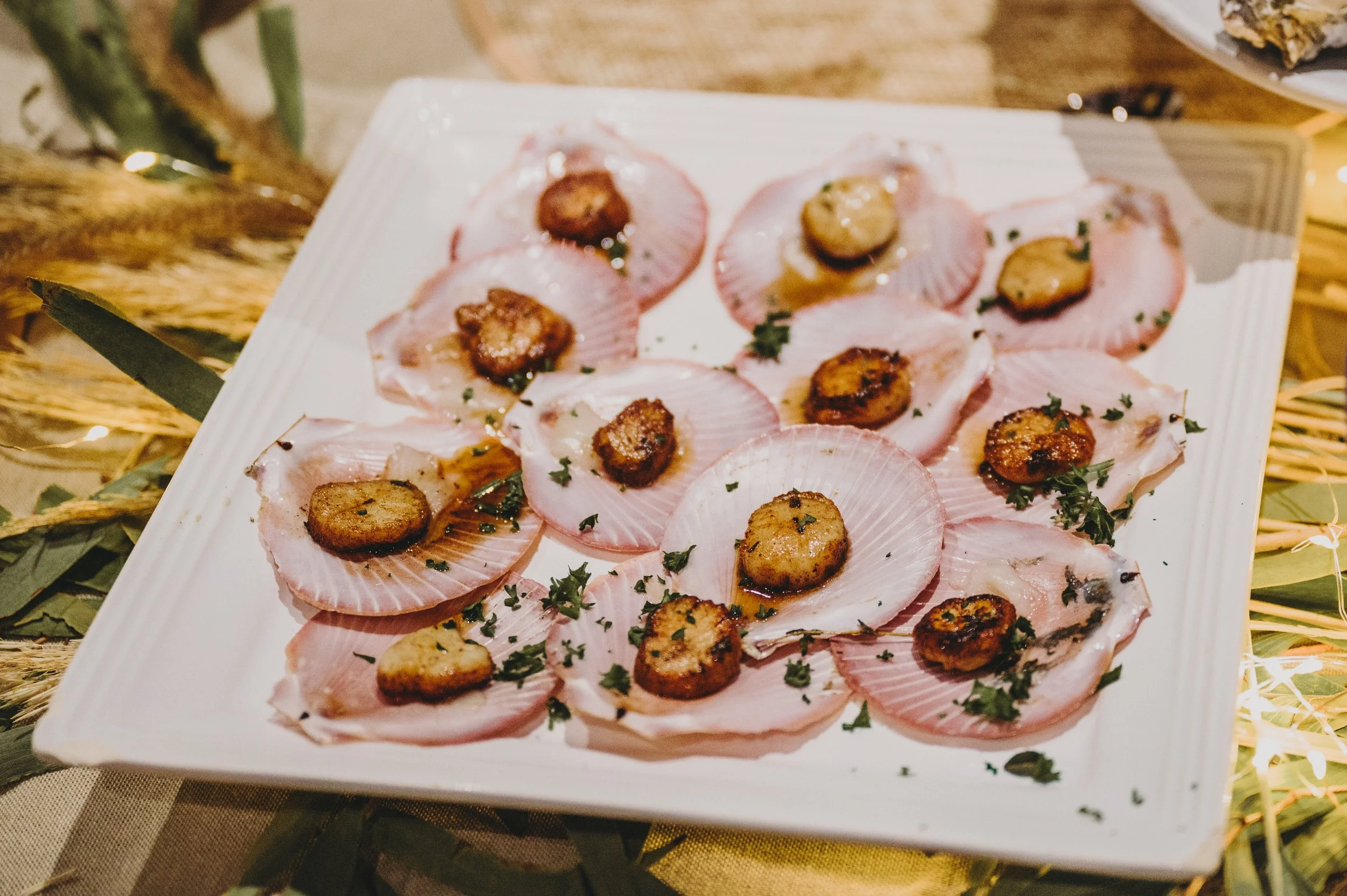 Plate of raw scallops topped with seared medallions and garnished with chopped herbs.