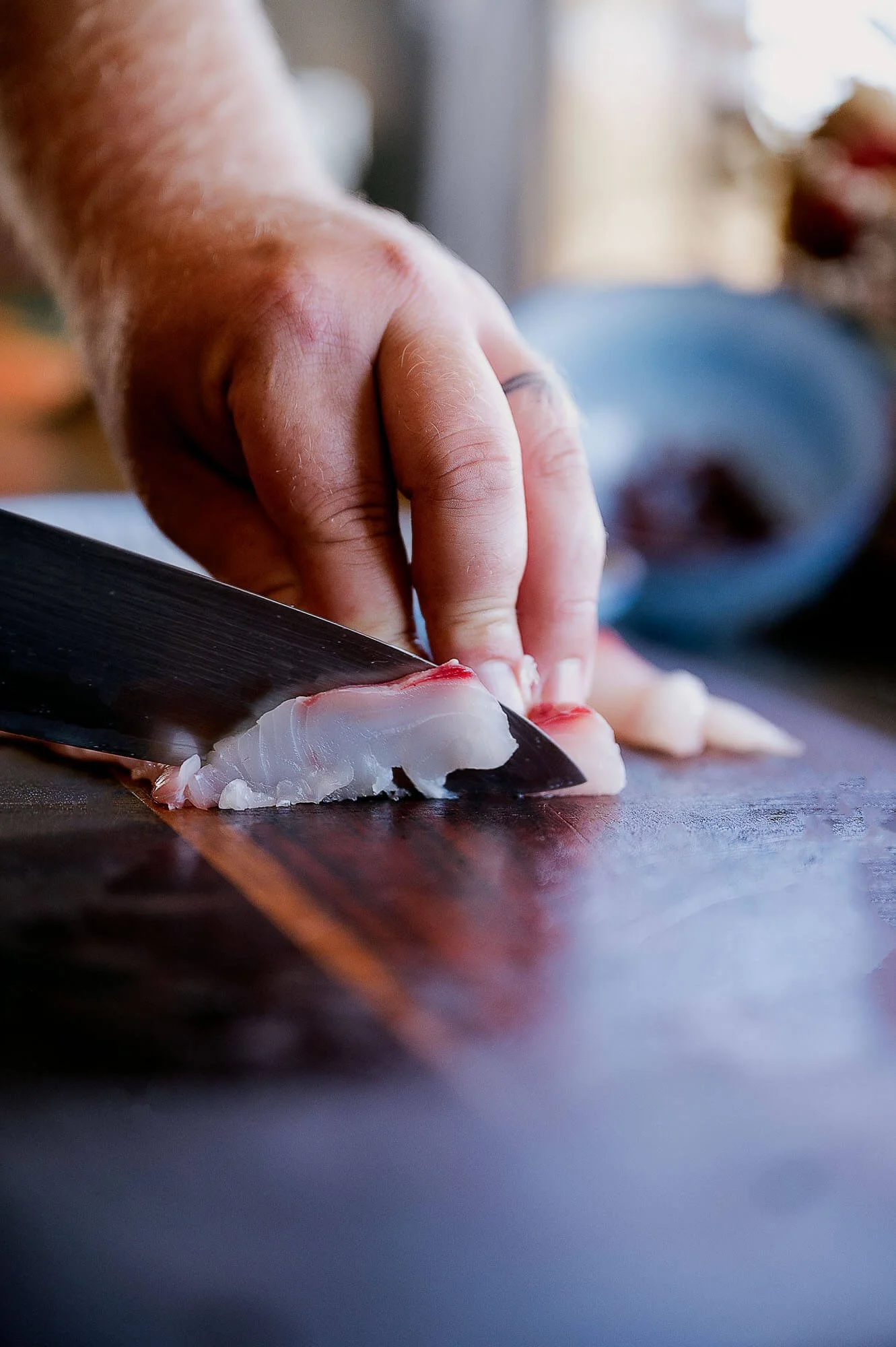 Close-up of a person slicing fish with a knife on a wooden cutting board in a kitchen.