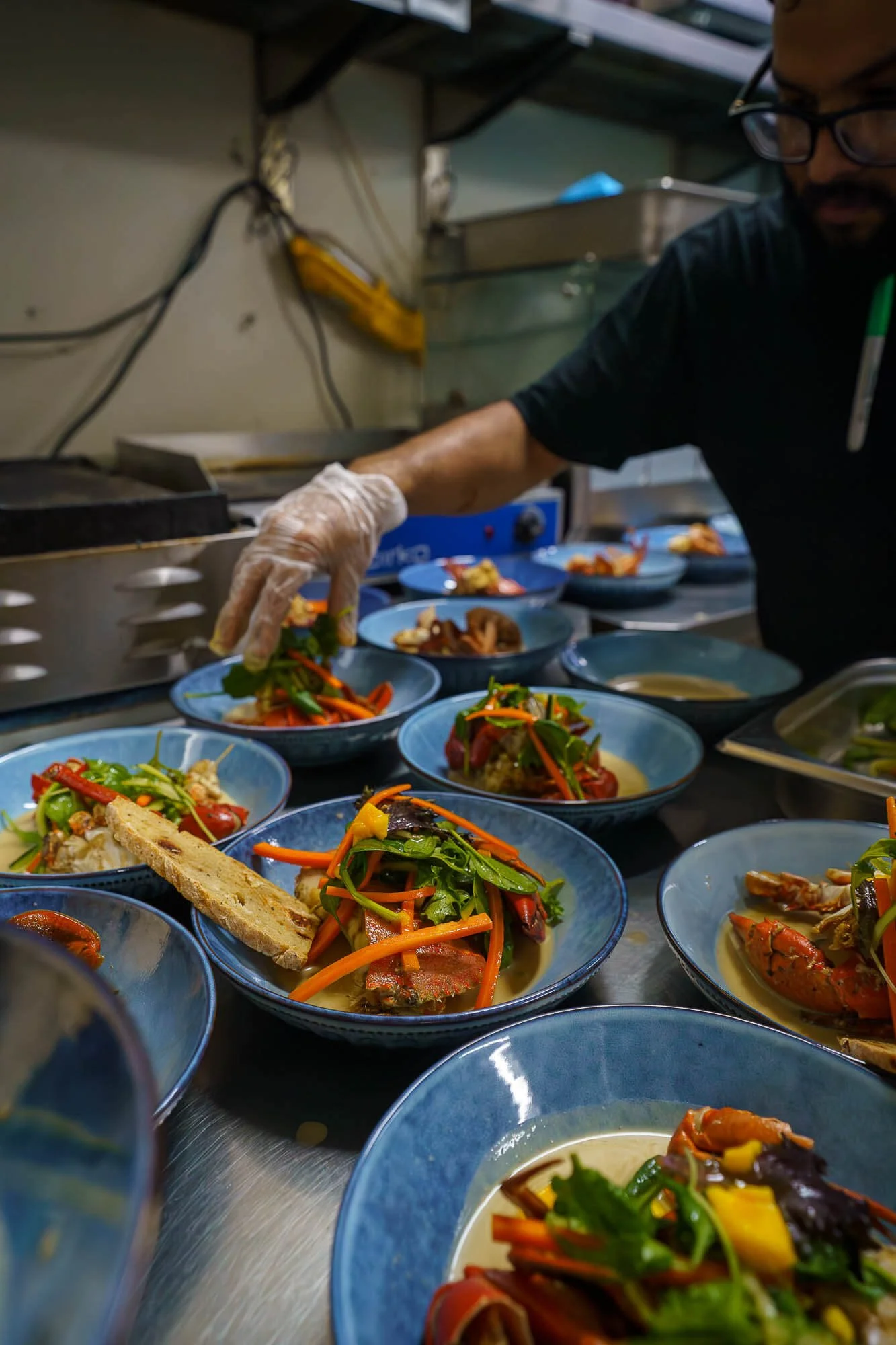 Chef preparing multiple dishes of seafood with vegetables in a professional kitchen.